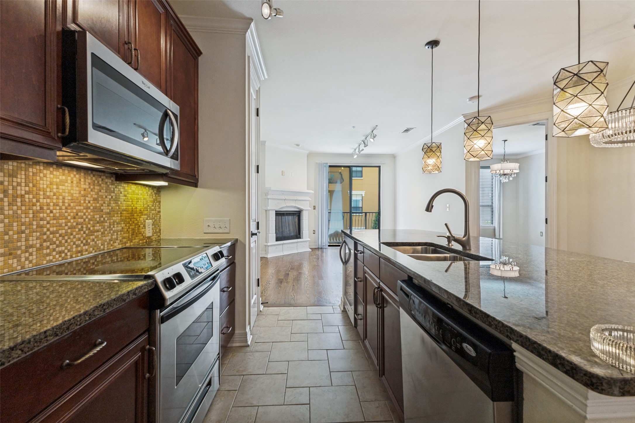 Condo kitchen with a granite island, double sink, dark wood cabinets, and mosaic tile backsplash.