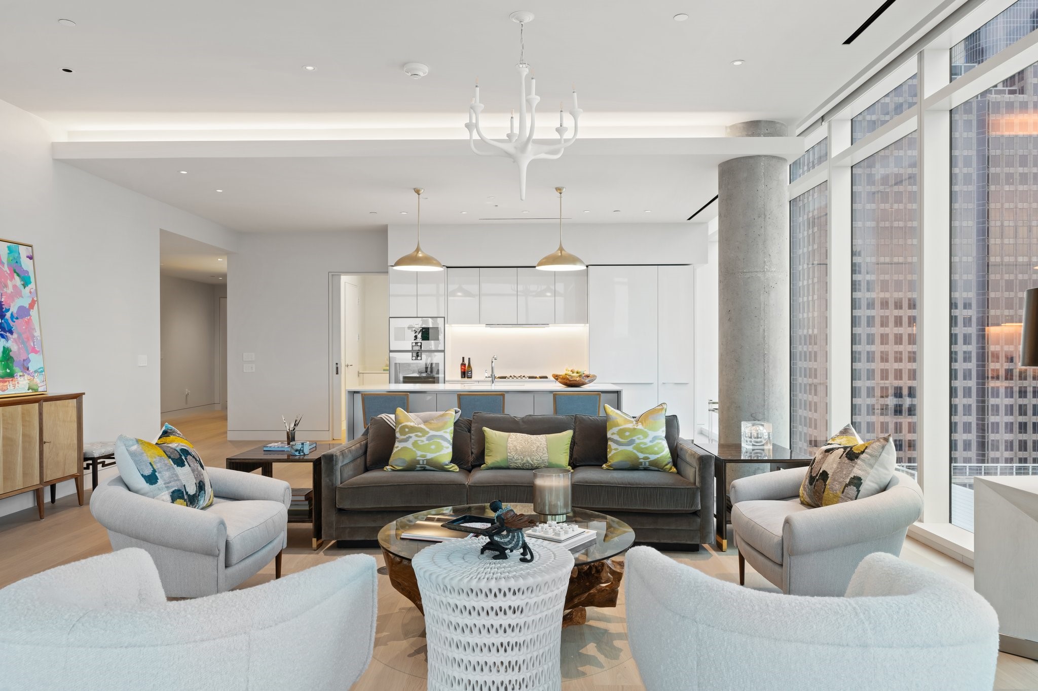 Staged condo living room with floor-to-ceiling city-view windows and an open white kitchen.