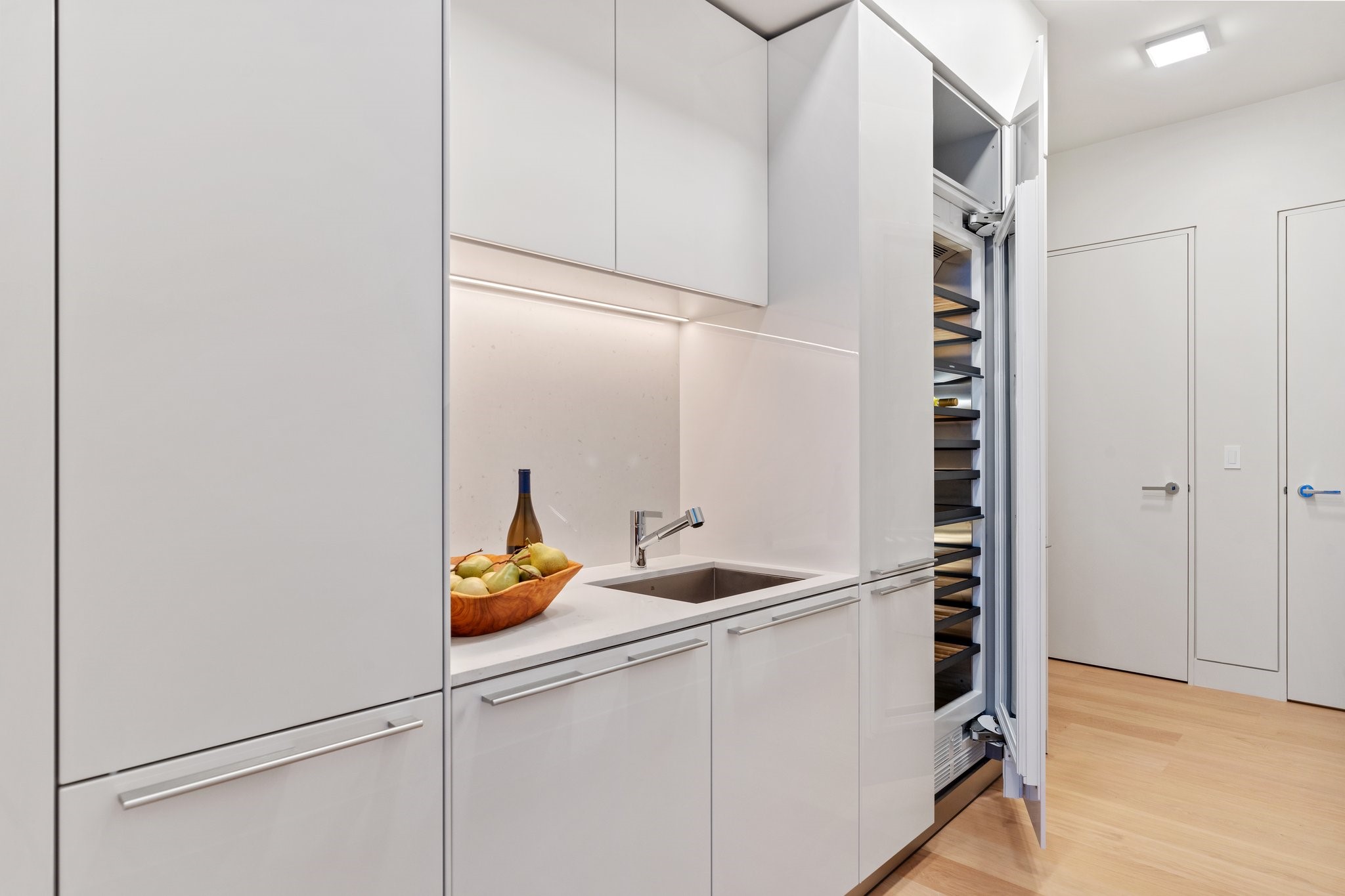 Modern white kitchen with a stone counter, undermount sink, and open built-in wine refrigerator.