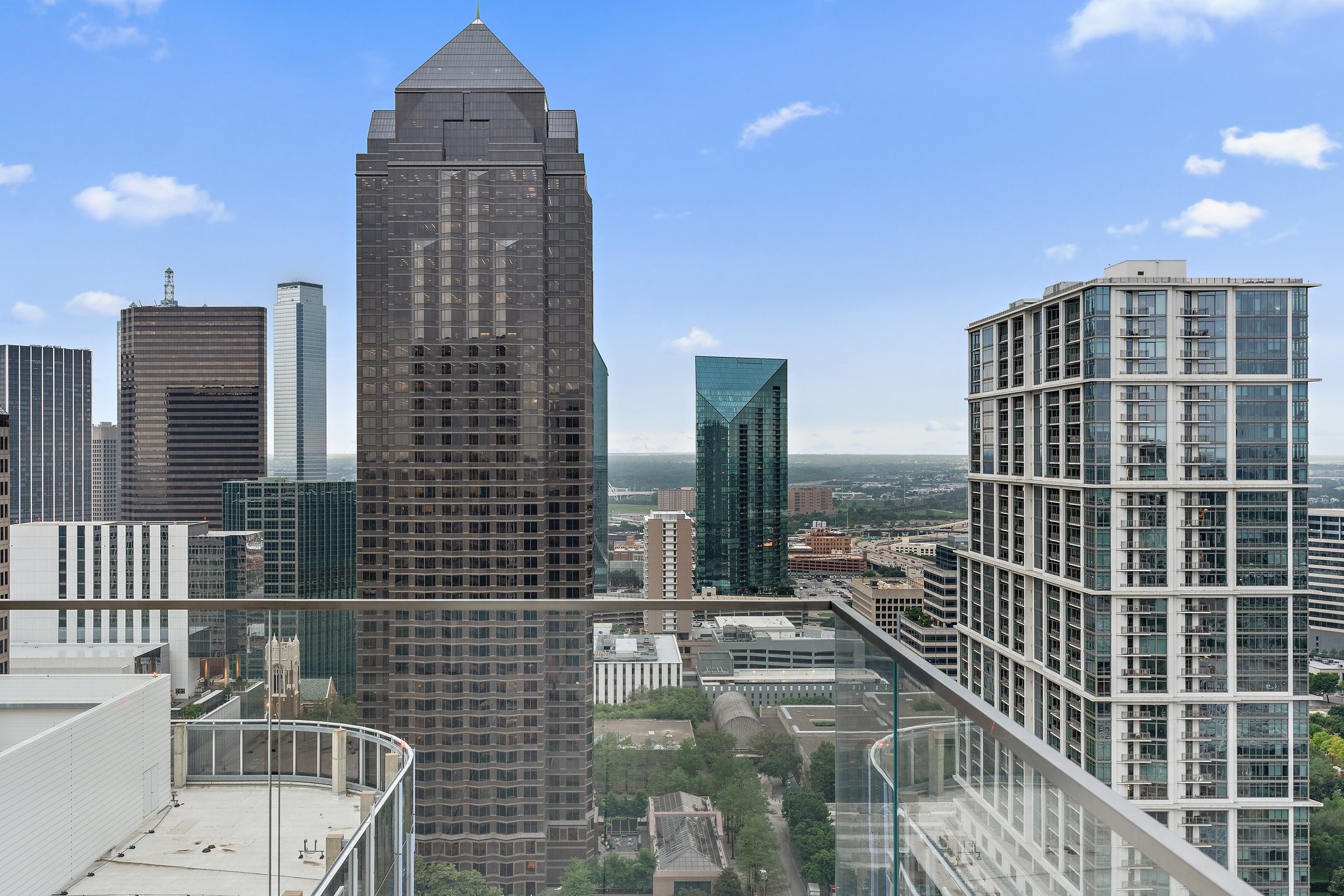 Downtown Dallas skyline viewed from a high-rise balcony with a glass railing.