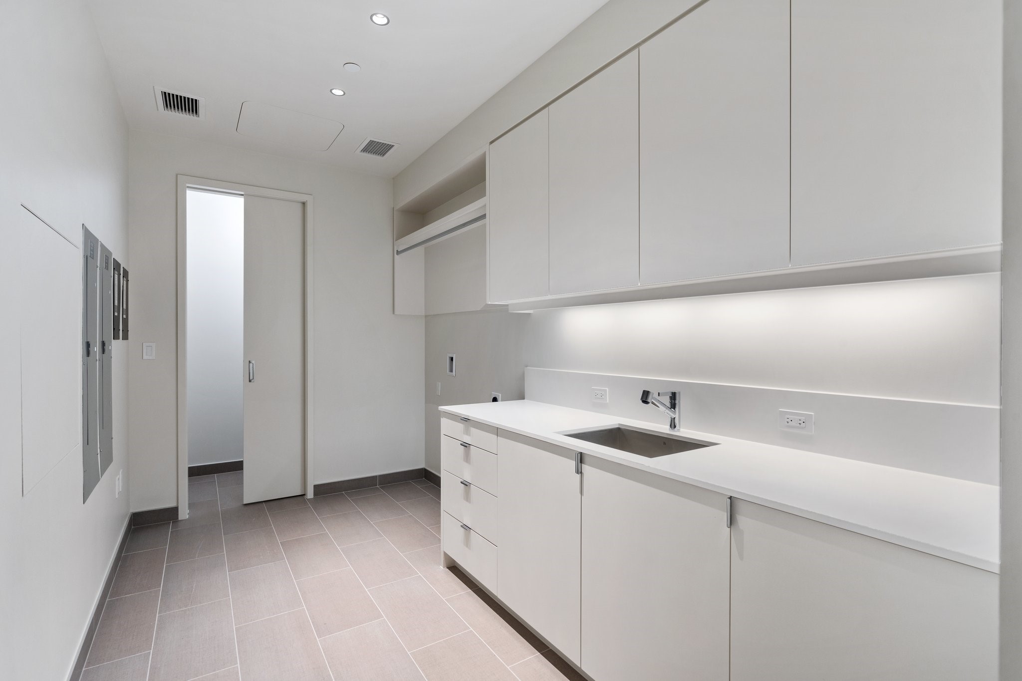 Vacant modern kitchen with white cabinets, a long counter, stainless steel sink, and gray tile floor.