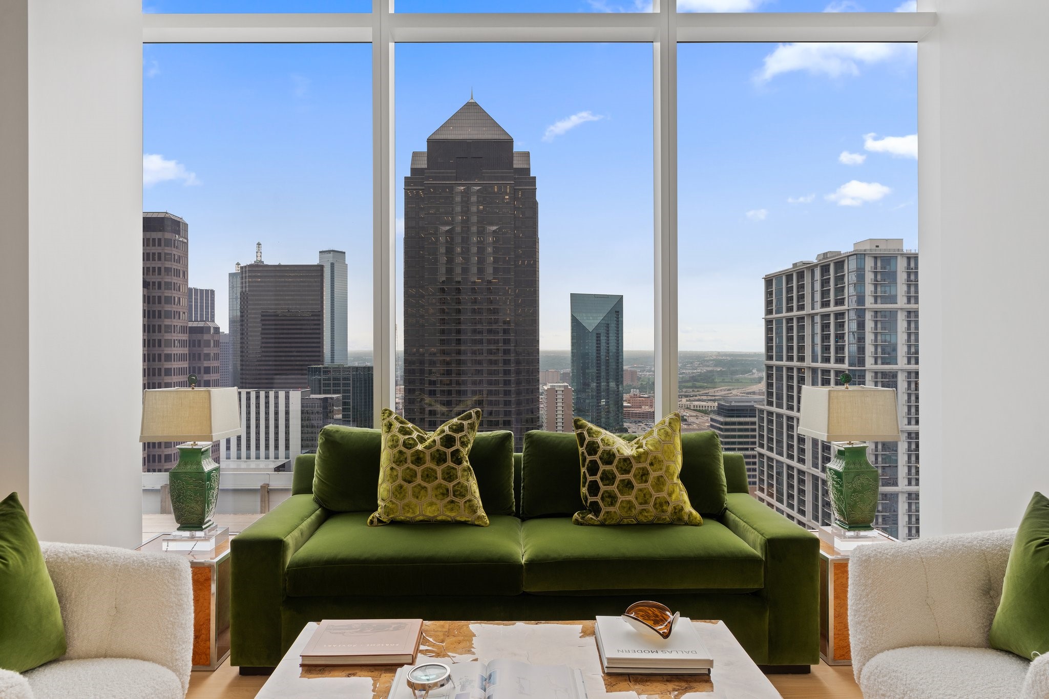 Staged living room with a green velvet sofa and floor-to-ceiling windows overlooking downtown Dallas.