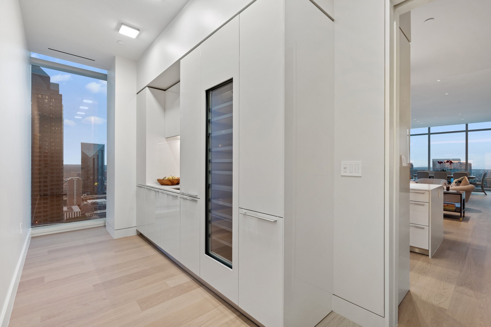 Modern condo kitchen with white cabinets and a glass-front wine refrigerator beside a downtown view.