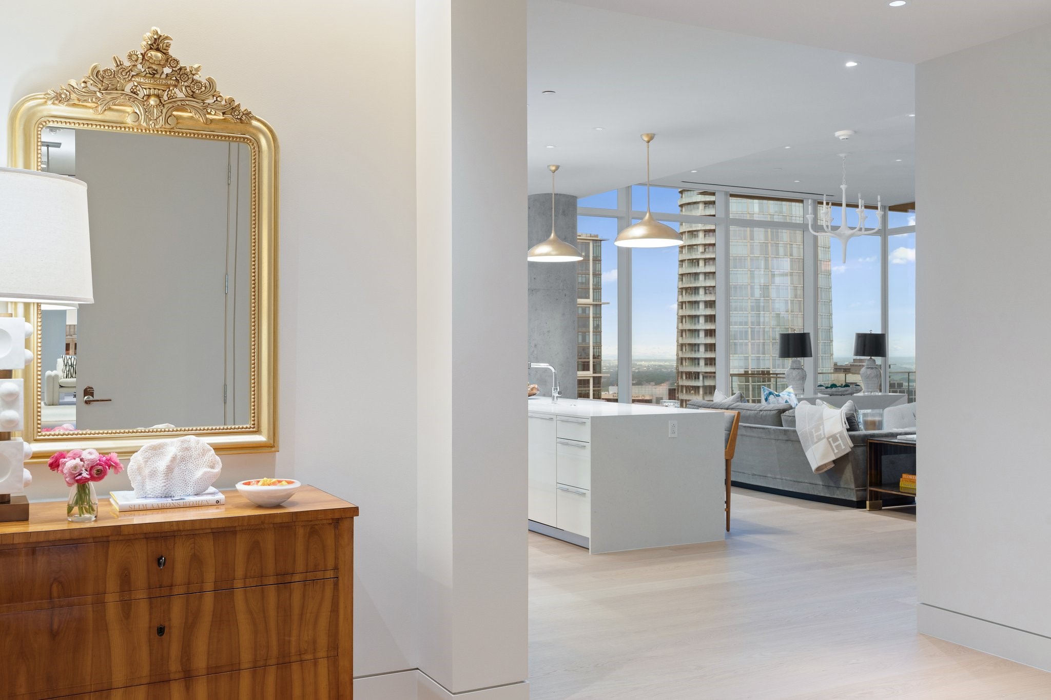 Furnished condo interior with an open kitchen, city-view living room, and ornate gold mirror above a wooden console.