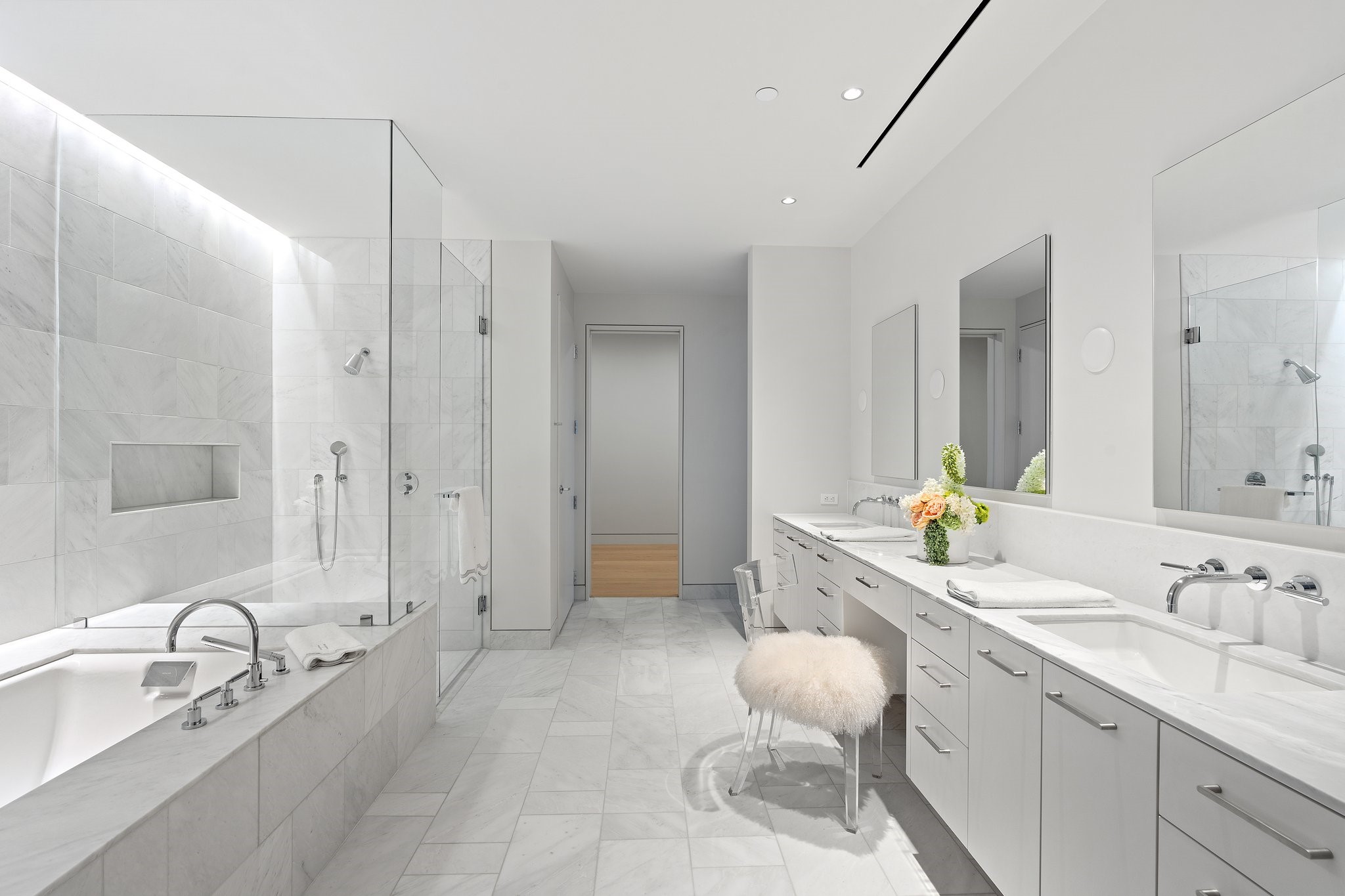 Modern marble bathroom with a glass shower, soaking tub, and long double-sink vanity.