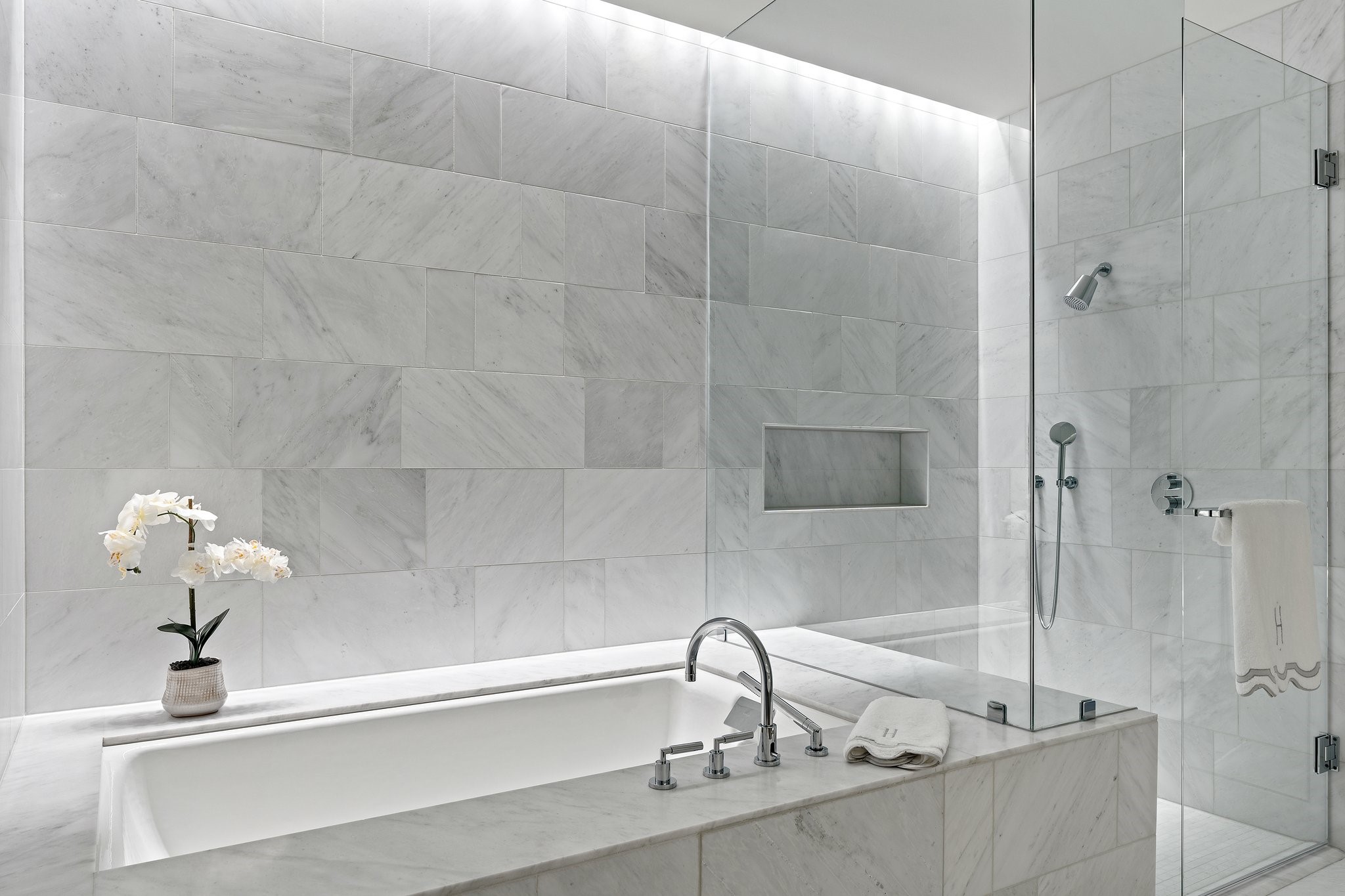 Marble bathroom with a built-in soaking tub, glass-enclosed shower, and white orchid.