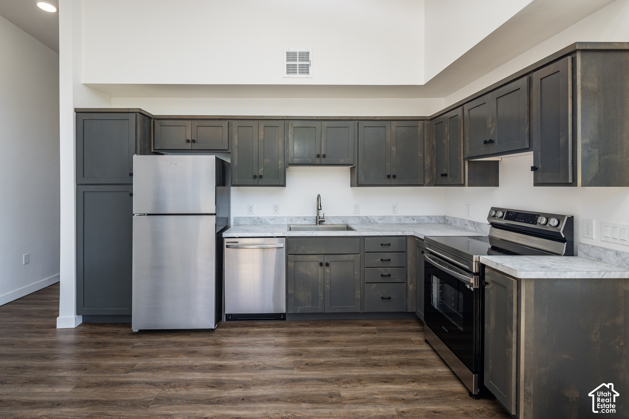 Kitchen with dark gray cabinets, stainless steel appliances, marble-look counters, and brown wood-look flooring.