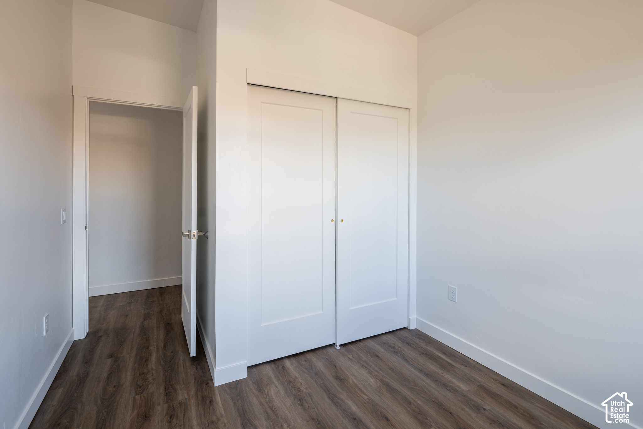 Vacant bedroom with dark wood-look flooring, a large white closet, and an open doorway.