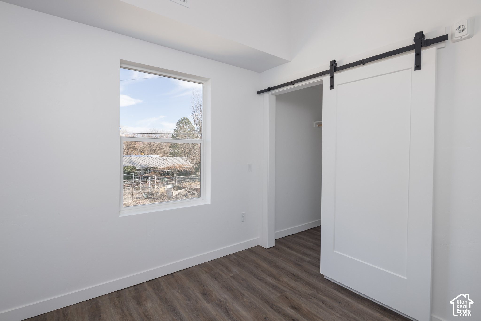 Vacant room with a large window, dark wood-look flooring, and a white sliding barn door.