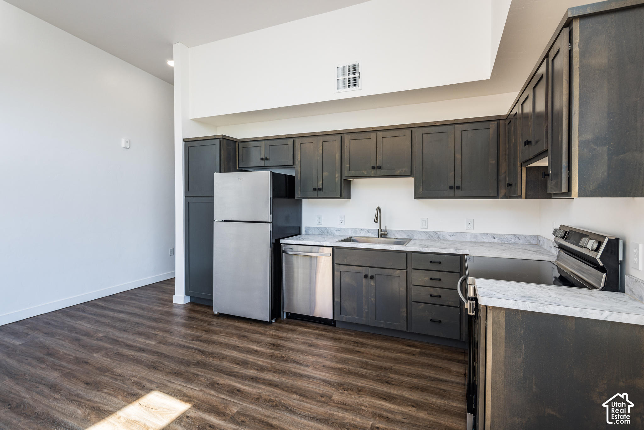 Modern kitchen with dark cabinets, marble-look counters, stainless steel appliances, and dark wood-look floors.