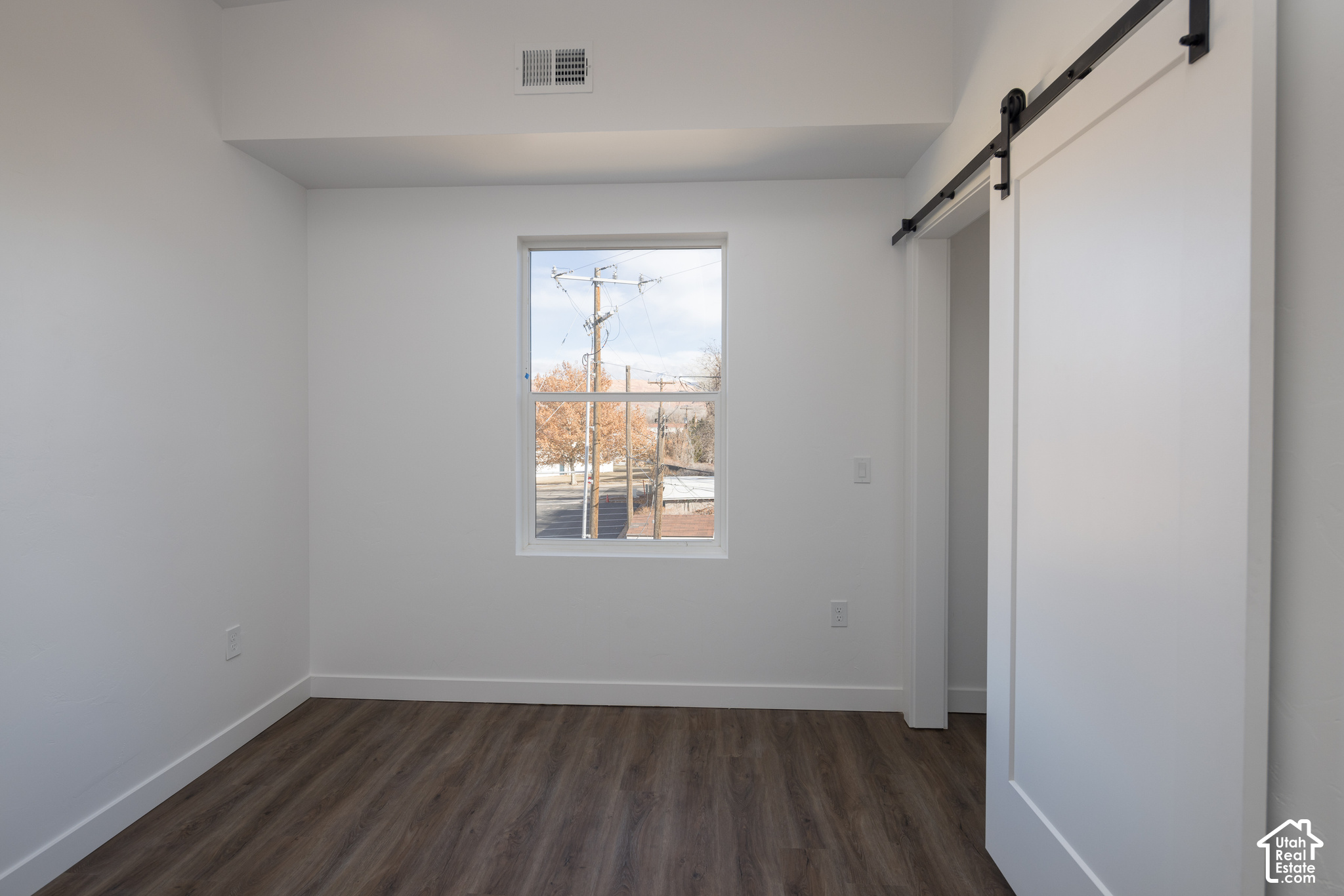 Empty bedroom with dark wood-look flooring, a window, and a white sliding barn-style door.