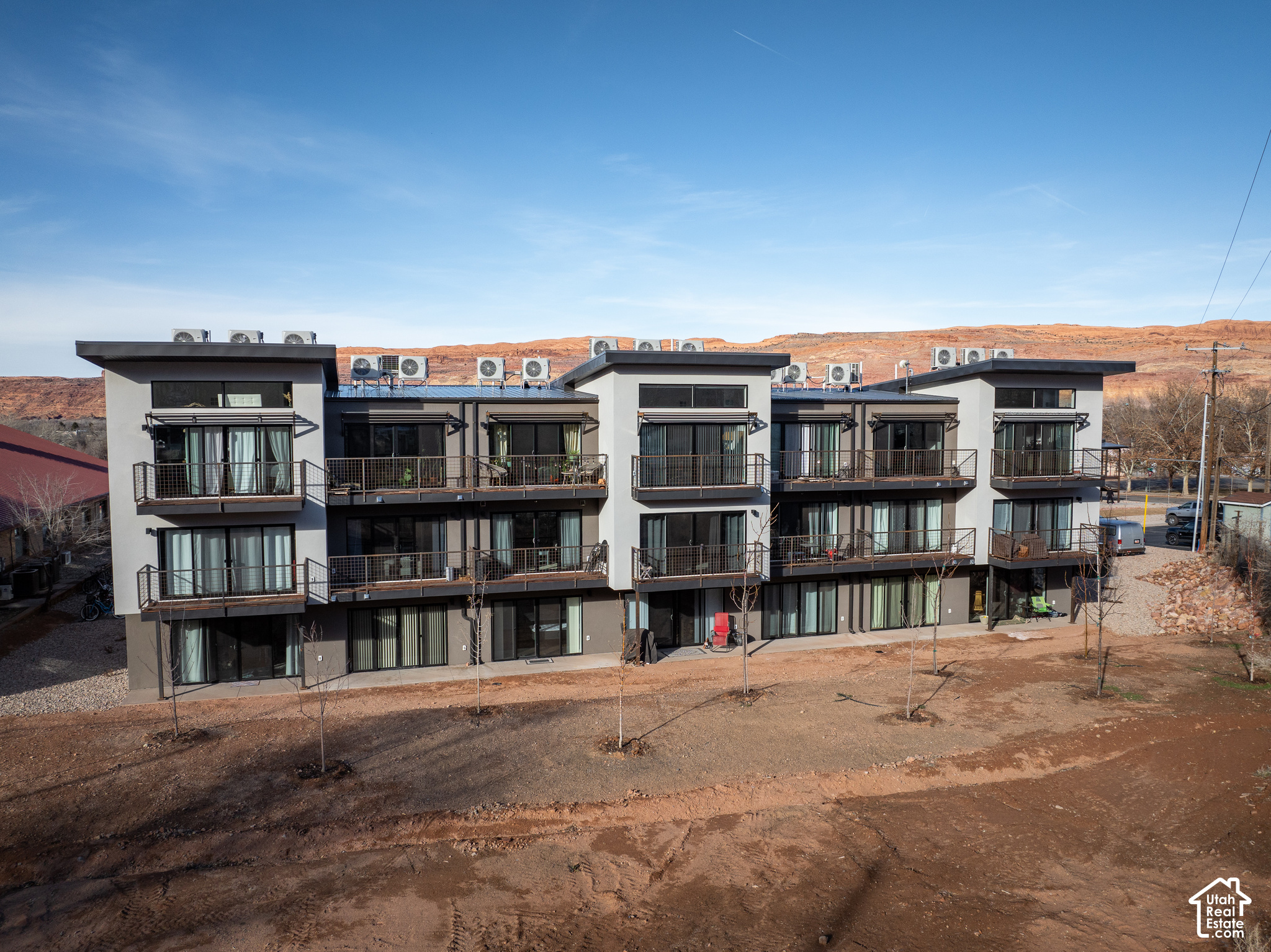 Modern multi-story condominium building with balconies, backed by red desert hills.