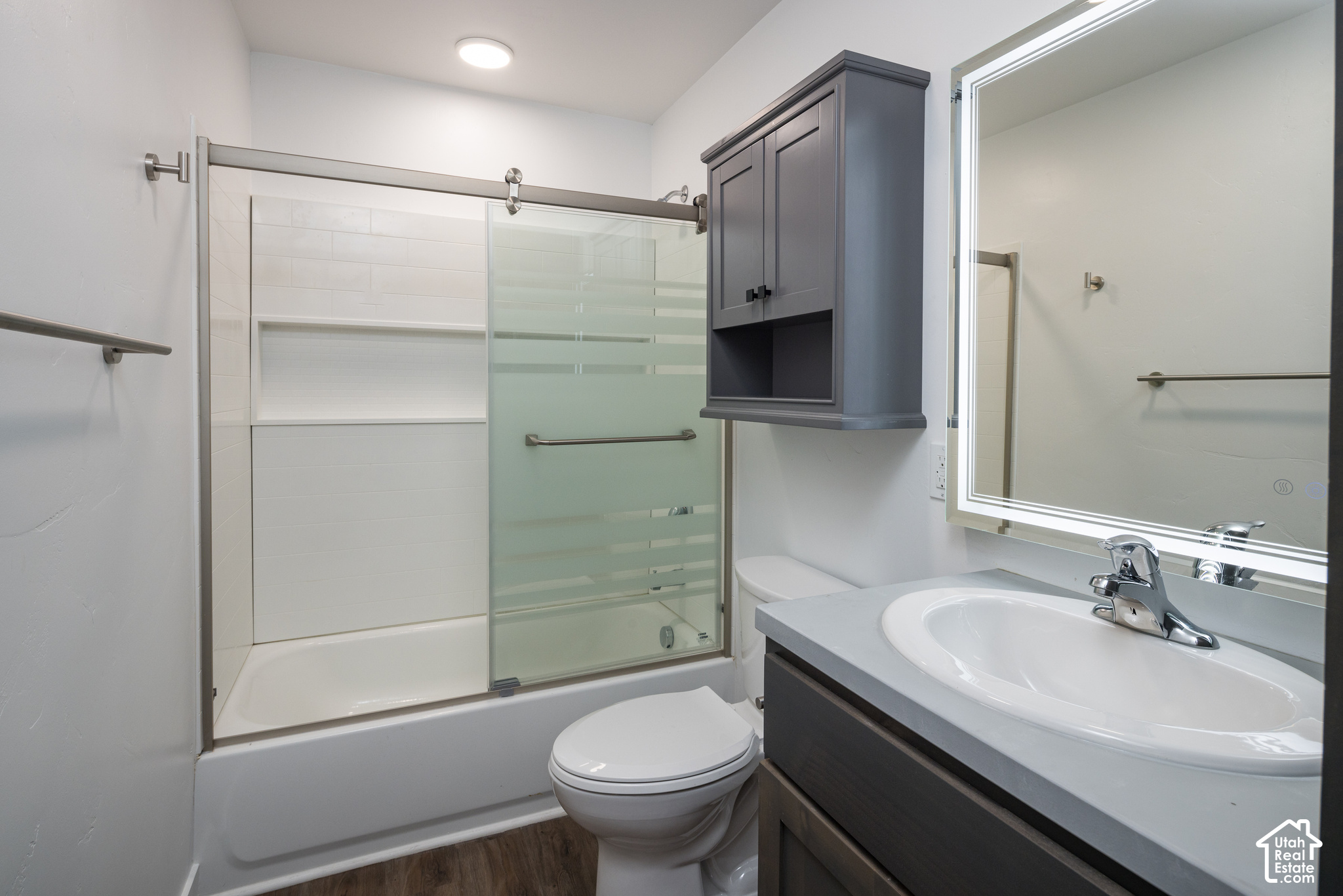 Bathroom with a glass-enclosed tub and shower, dark vanity, and illuminated mirror.