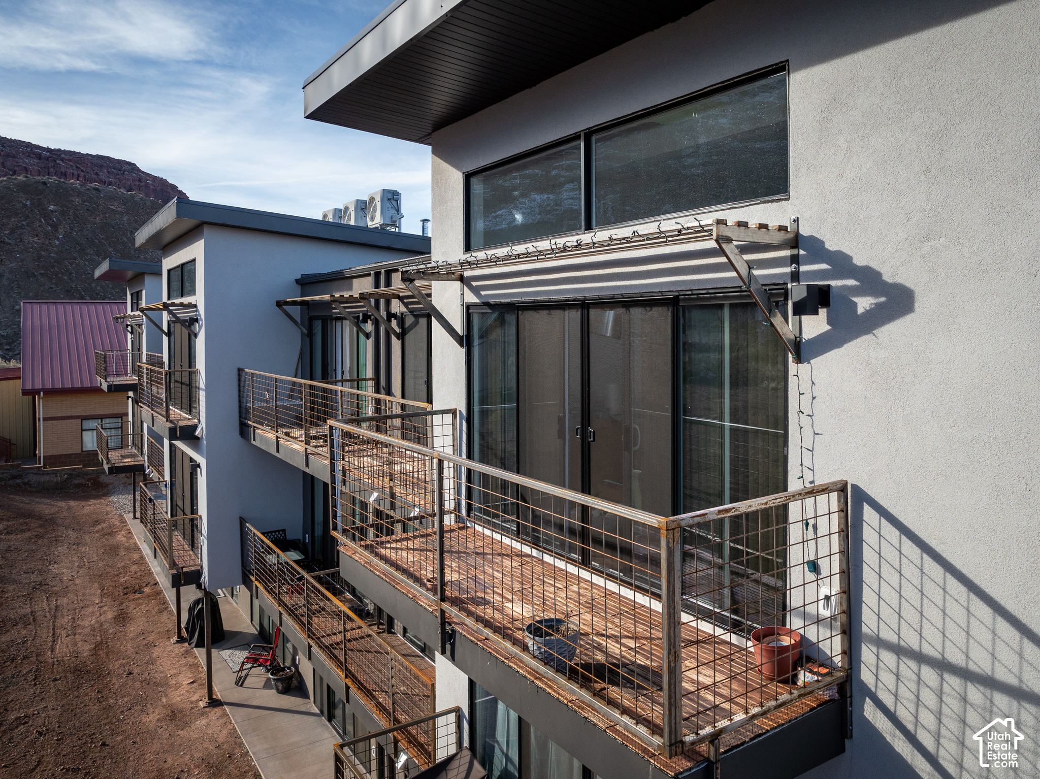 Modern Moab building with wood-deck balconies and metal railings below a rocky red ridge.