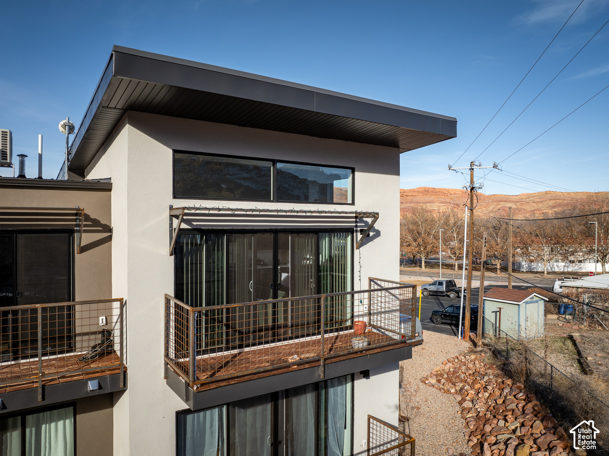 Modern white building with metal-railed balconies, backed by red rock hills.