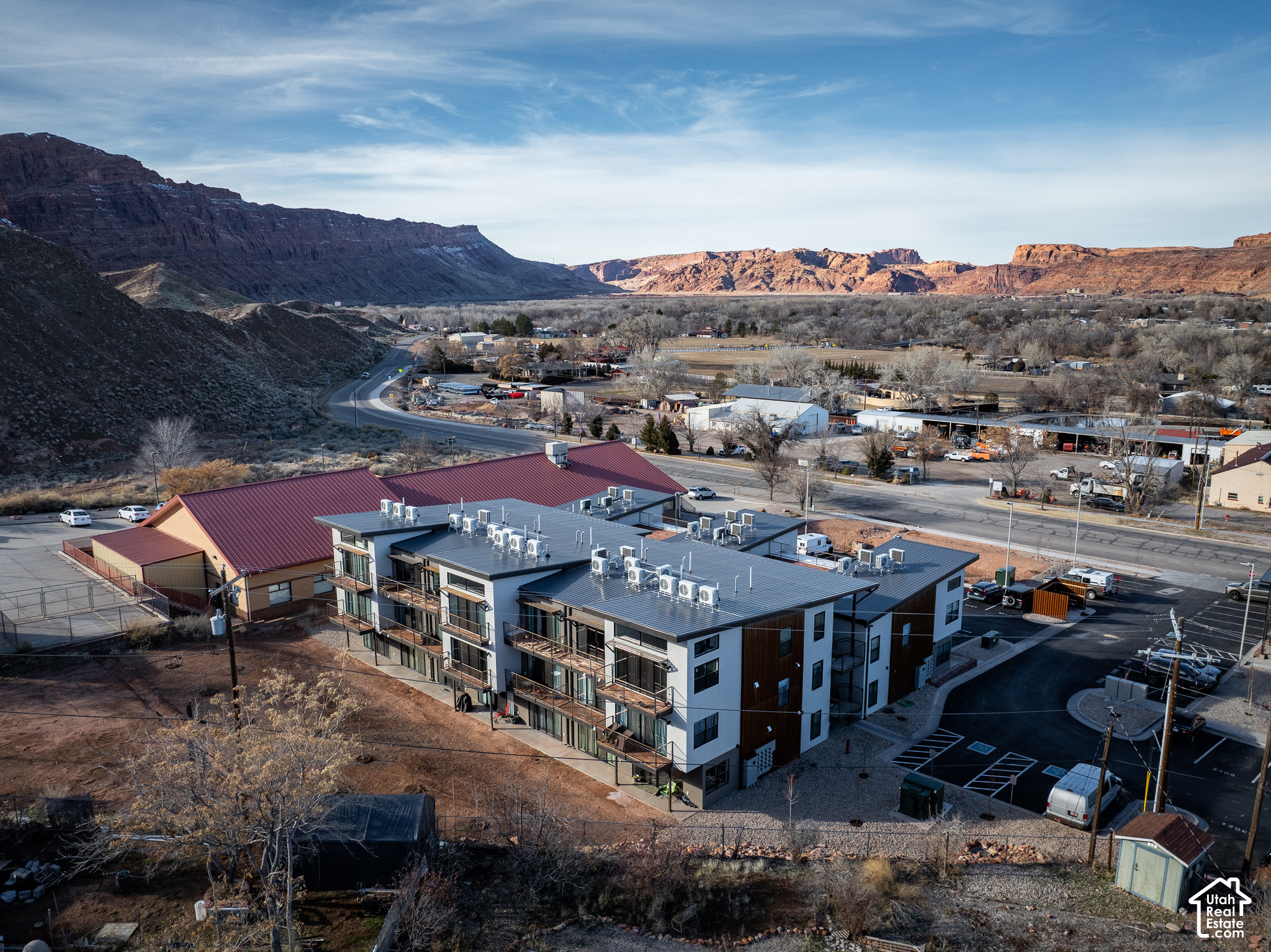 Aerial view of a modern apartment building with balconies, parking, and red-rock mountains beyond.