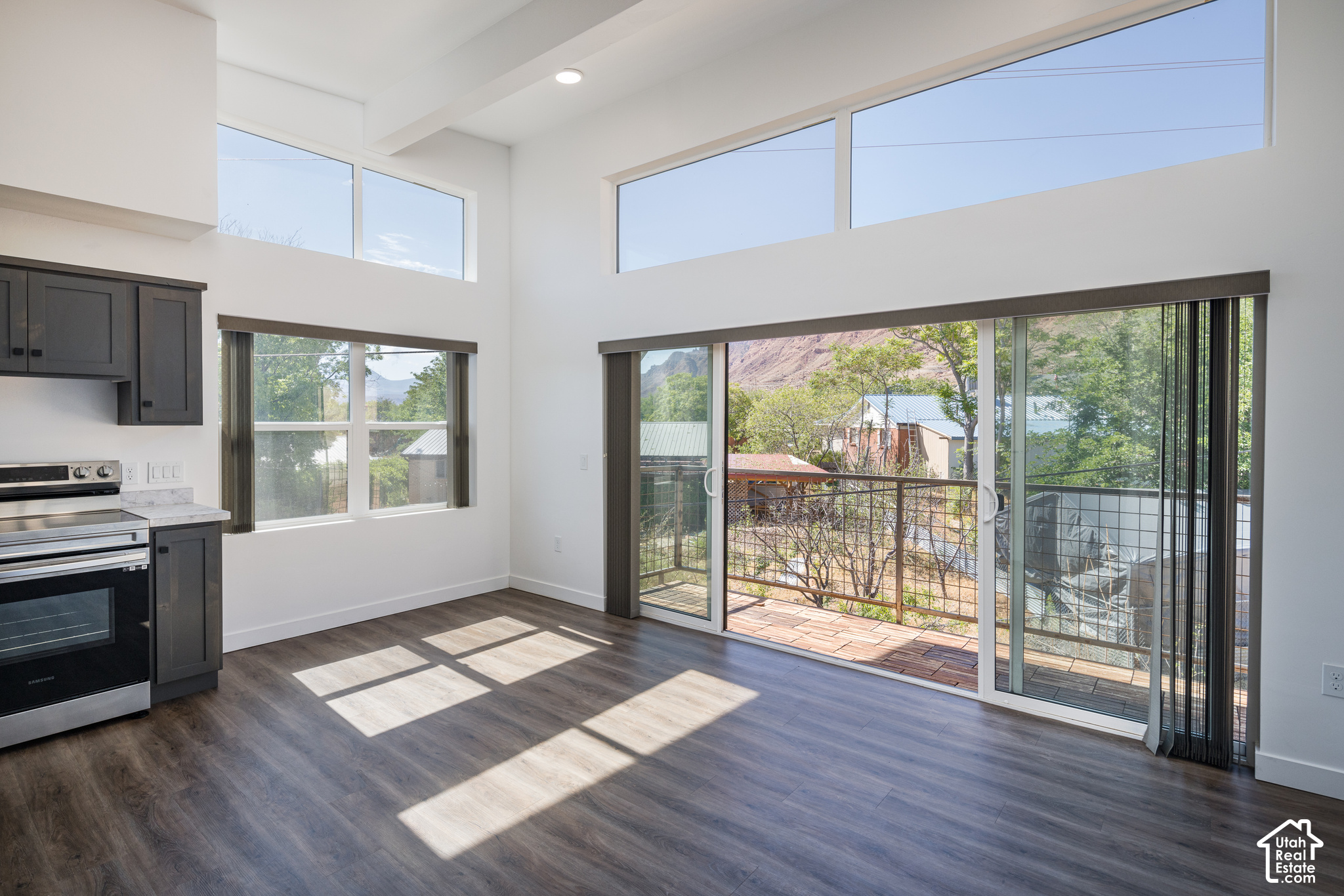 Vacant living area with tall windows opening to a balcony and views of trees and red-rock terrain.