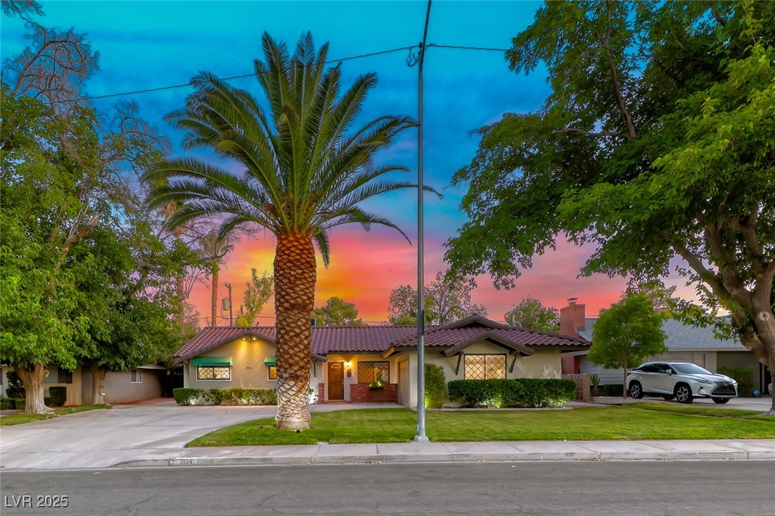 Single-story stucco home with a tile roof and tall palm tree at dusk.