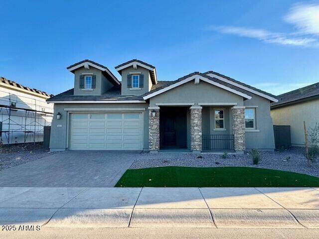Gray stucco home with stone accents, two dormers, a two-car garage, and a small front lawn.