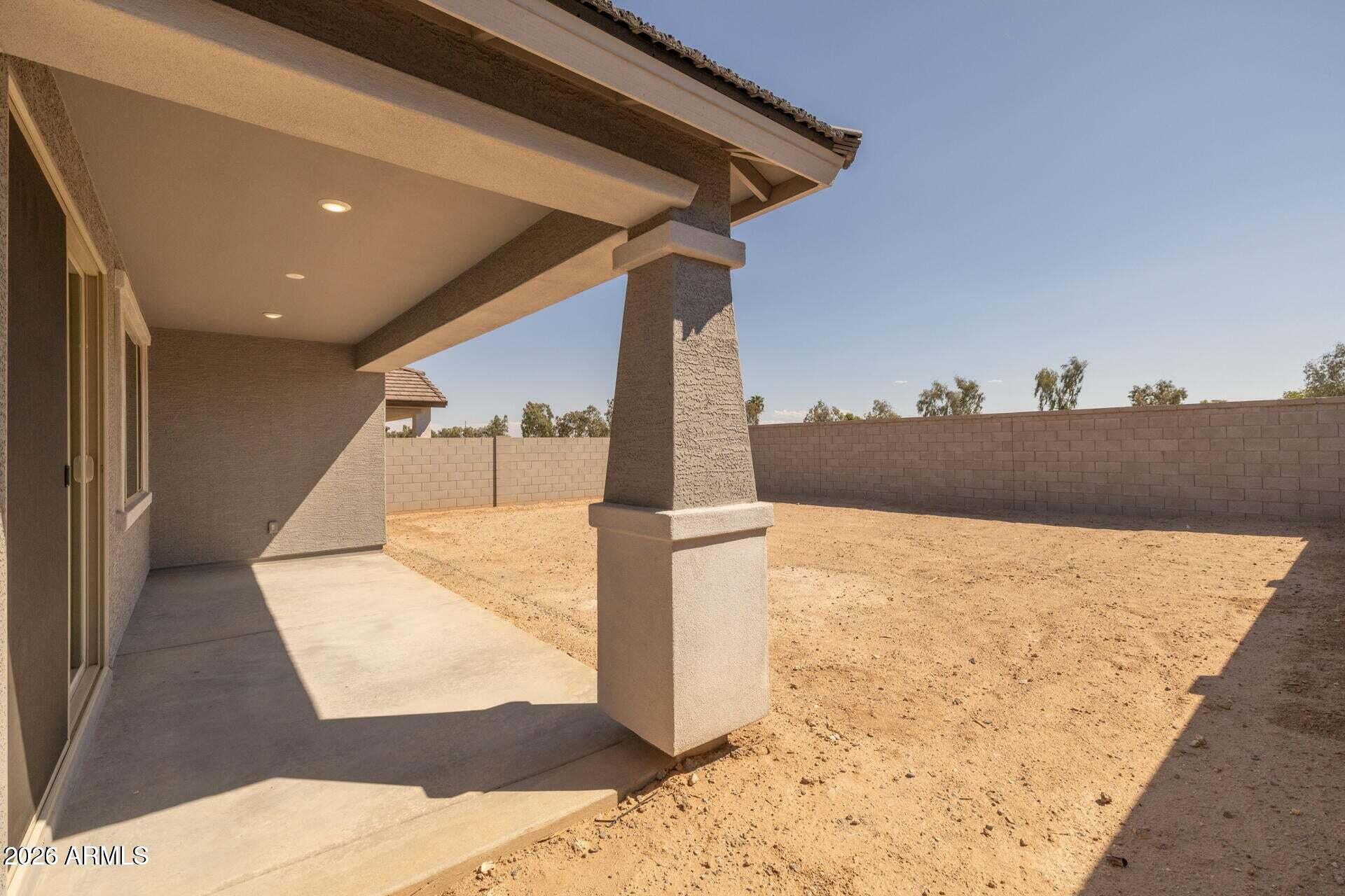 Covered concrete patio beside a bare dirt backyard enclosed by a block wall.