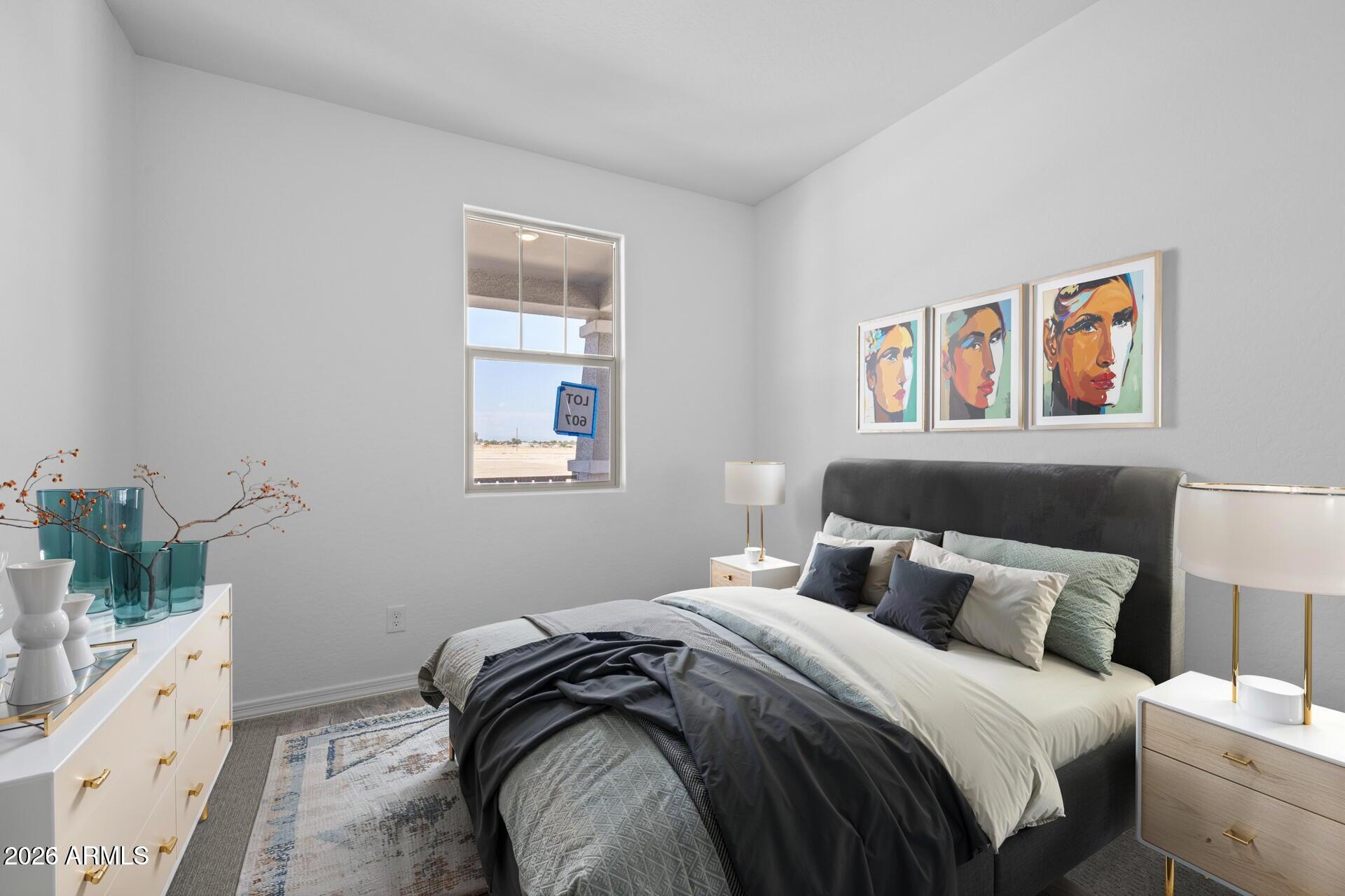 Staged bedroom with a dark upholstered bed, colorful portrait prints, and a window overlooking open land.