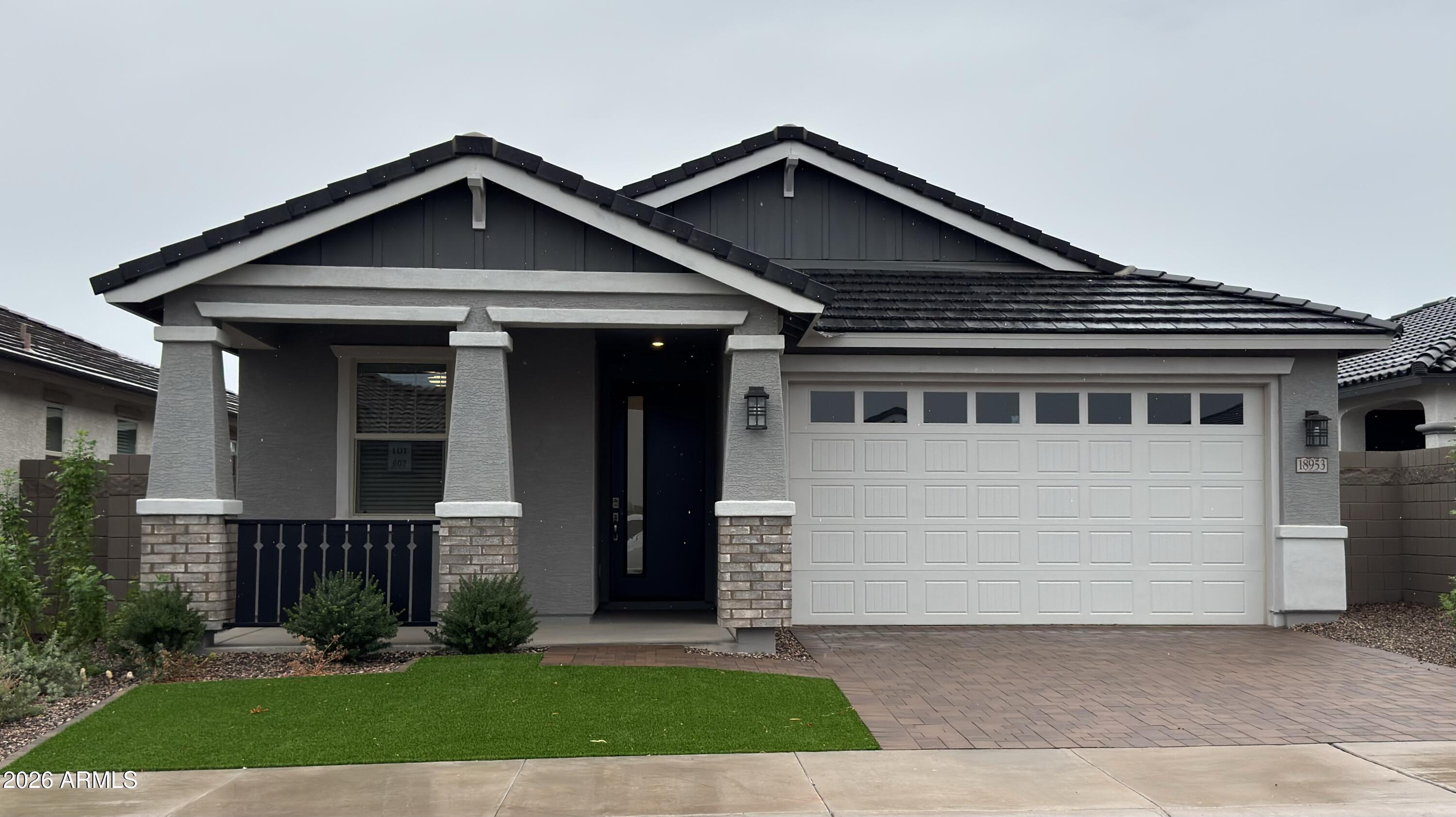 Gray single-story home with a covered porch, white garage door, and brick-paver driveway.