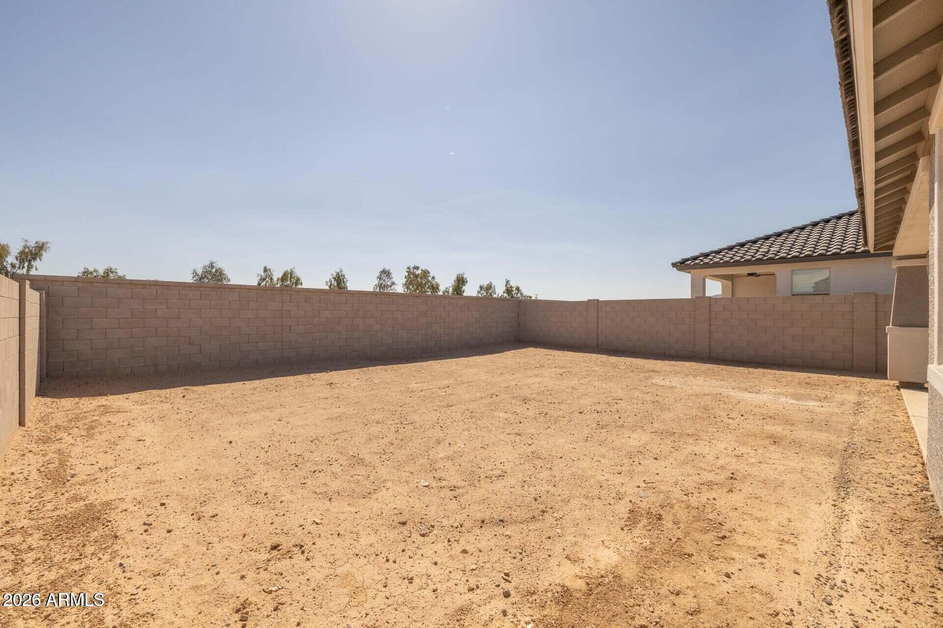 Bare dirt backyard enclosed by tan block walls, with the home’s covered patio at right.