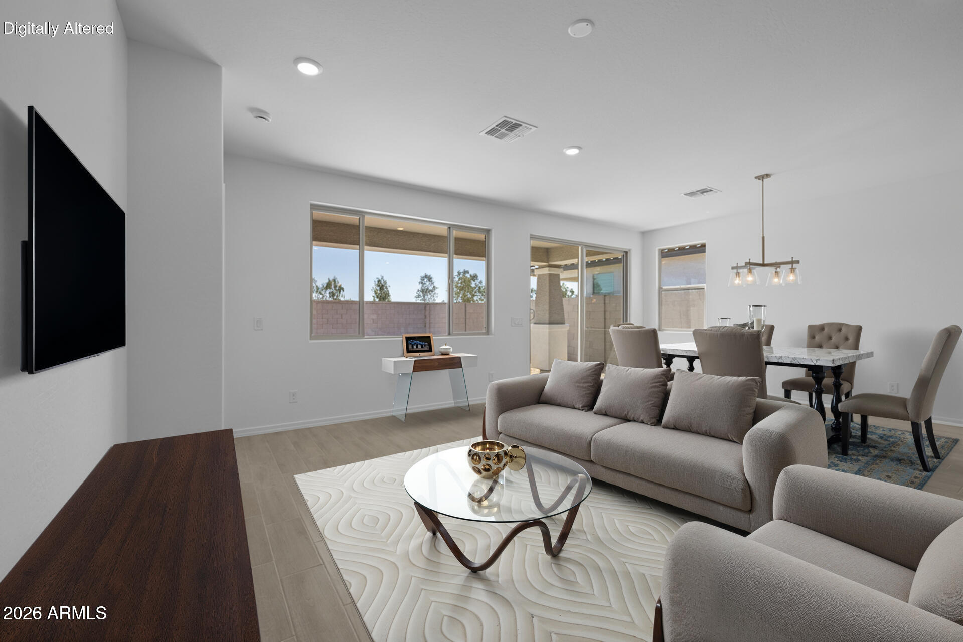 Living and dining room with gray seating, a glass coffee table, and large windows overlooking a walled yard.