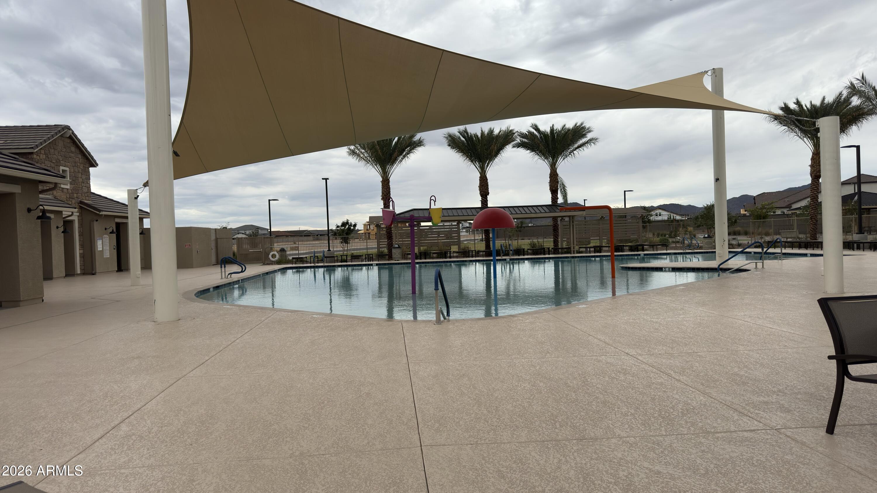 Community pool with colorful splash features beneath a broad shade sail and palm trees.