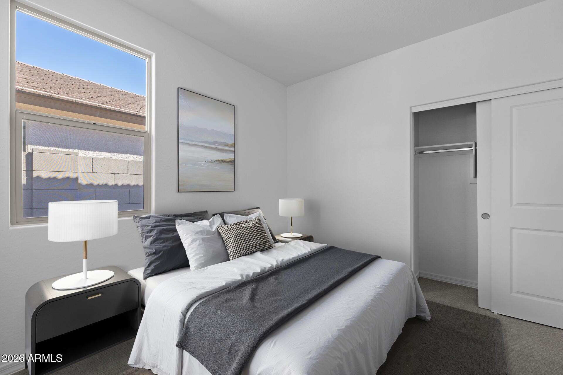 Staged bedroom with a white bed, charcoal throw, large window, and open closet.
