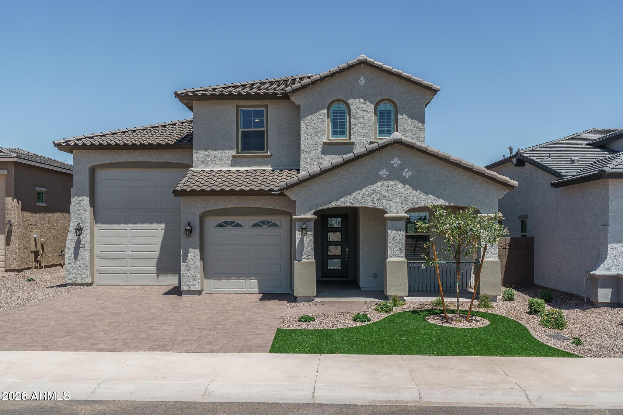 Two-story stucco home with a tiled roof, two garage doors, and desert landscaping.