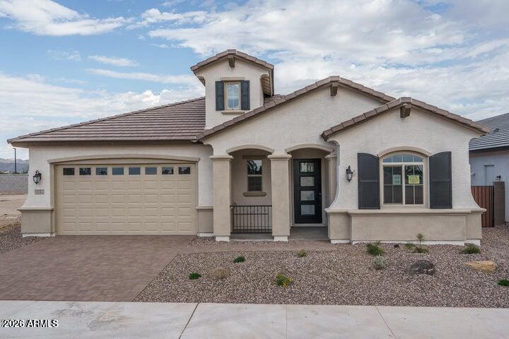 Beige stucco home with a two-car garage, tiled roof, and gravel desert landscaping.