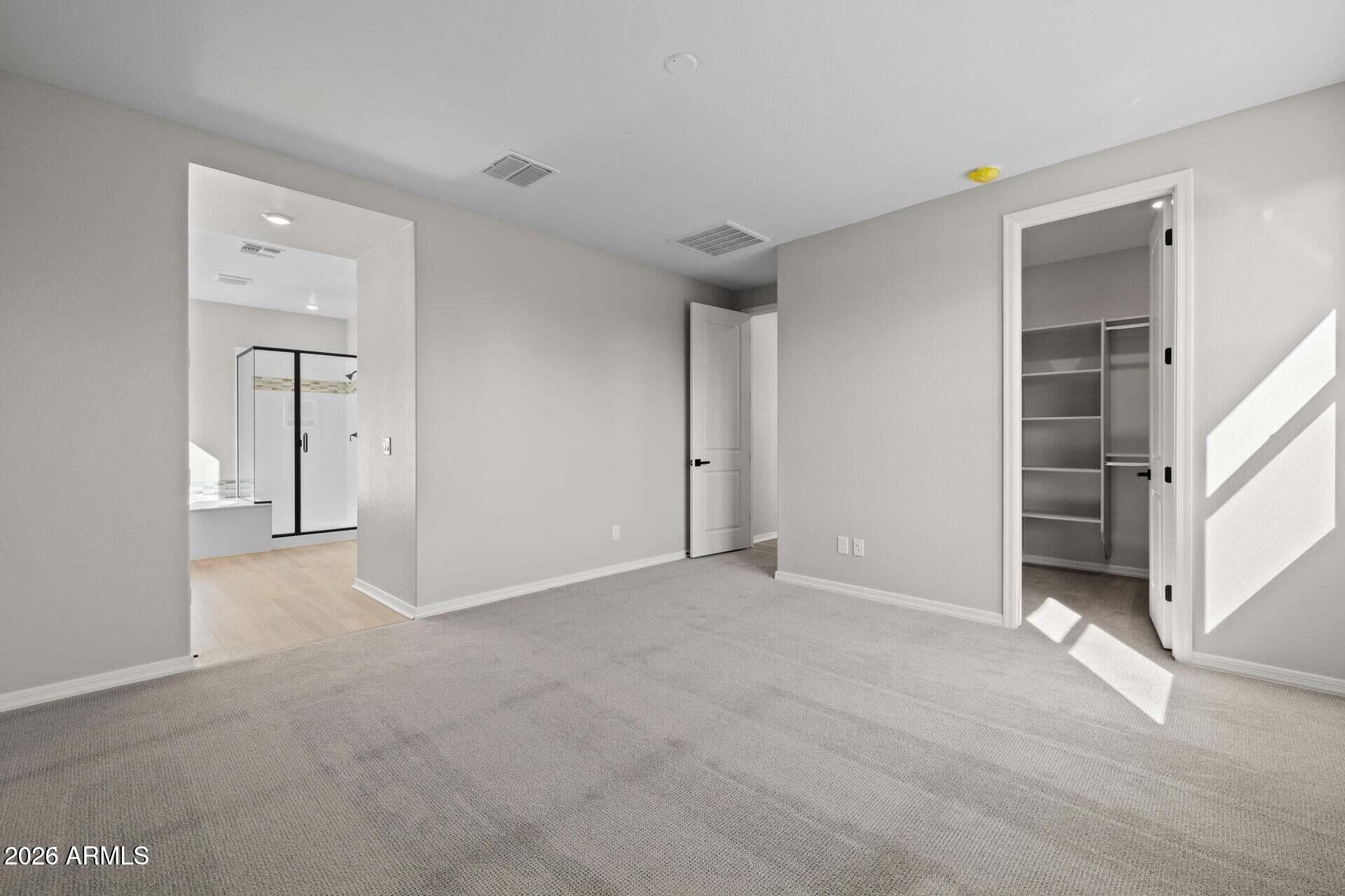 Empty carpeted bedroom with an open walk-in closet and a bathroom doorway; sunlight streams across the floor.