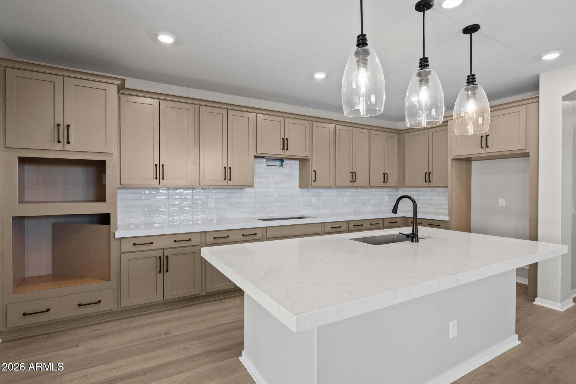 Unfurnished kitchen with a large white island, taupe cabinetry, and three glass pendant lights.