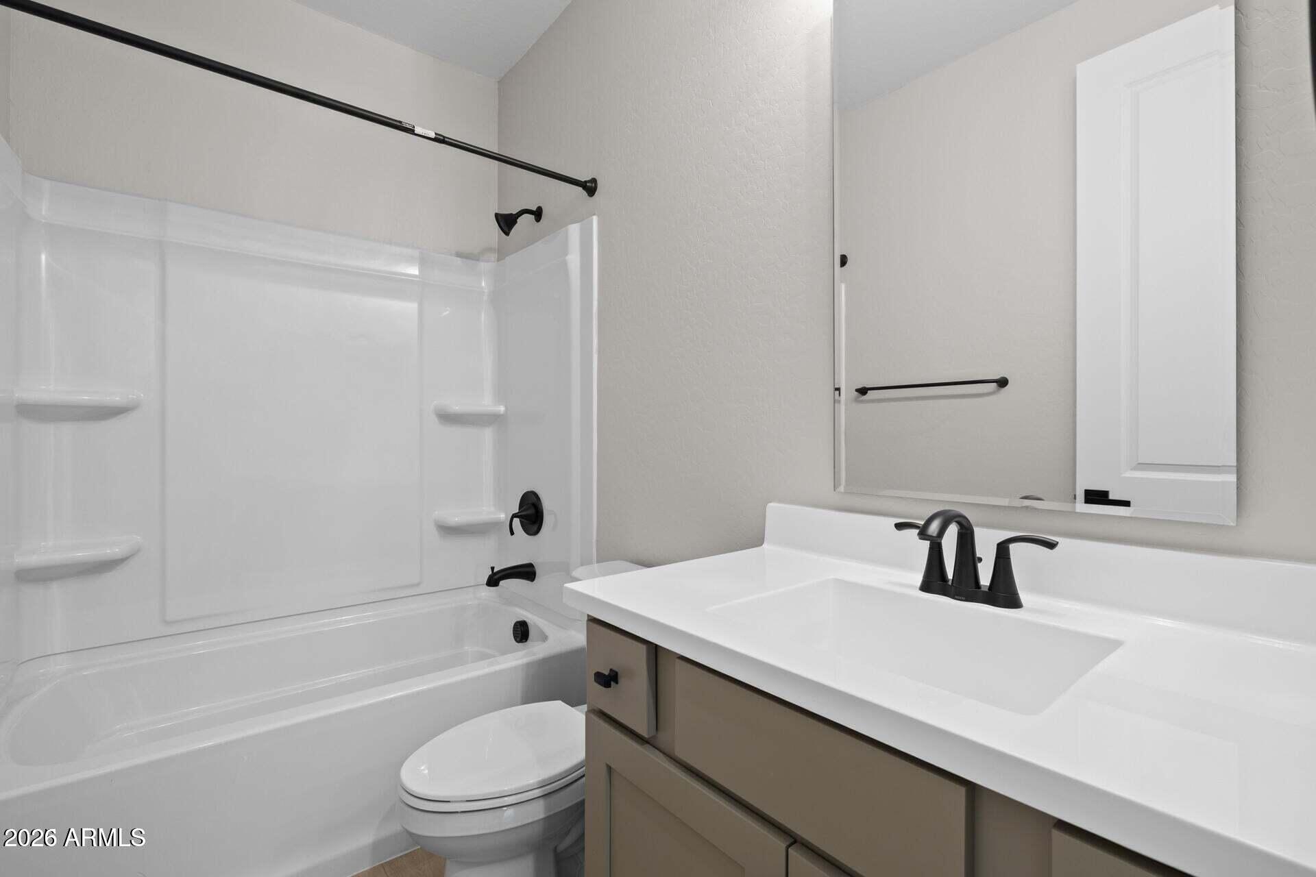 Bathroom with a white tub and shower beside a taupe vanity with black fixtures.