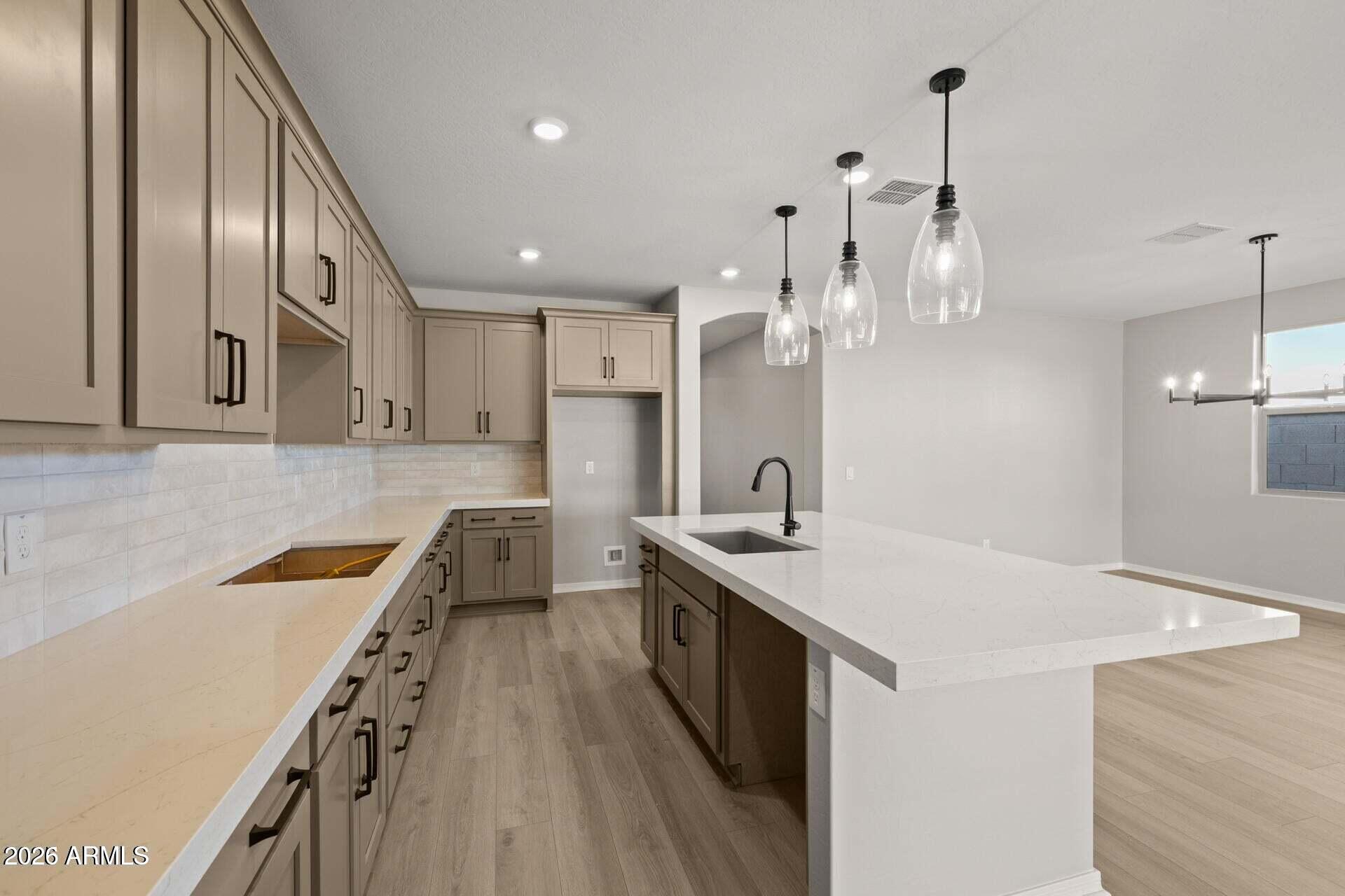 Kitchen with taupe cabinets, white countertops, and a large island with a sink.