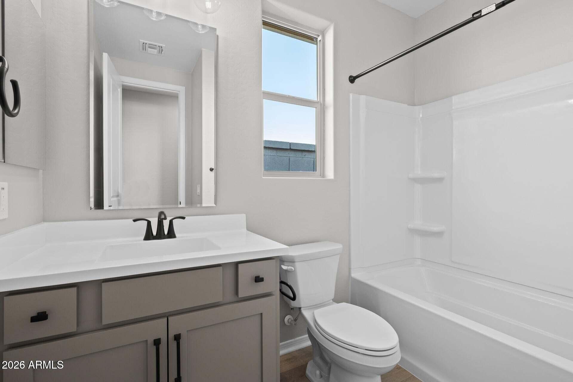 Bathroom with gray vanity, black faucet, white toilet, and tub-shower beside a tall window.