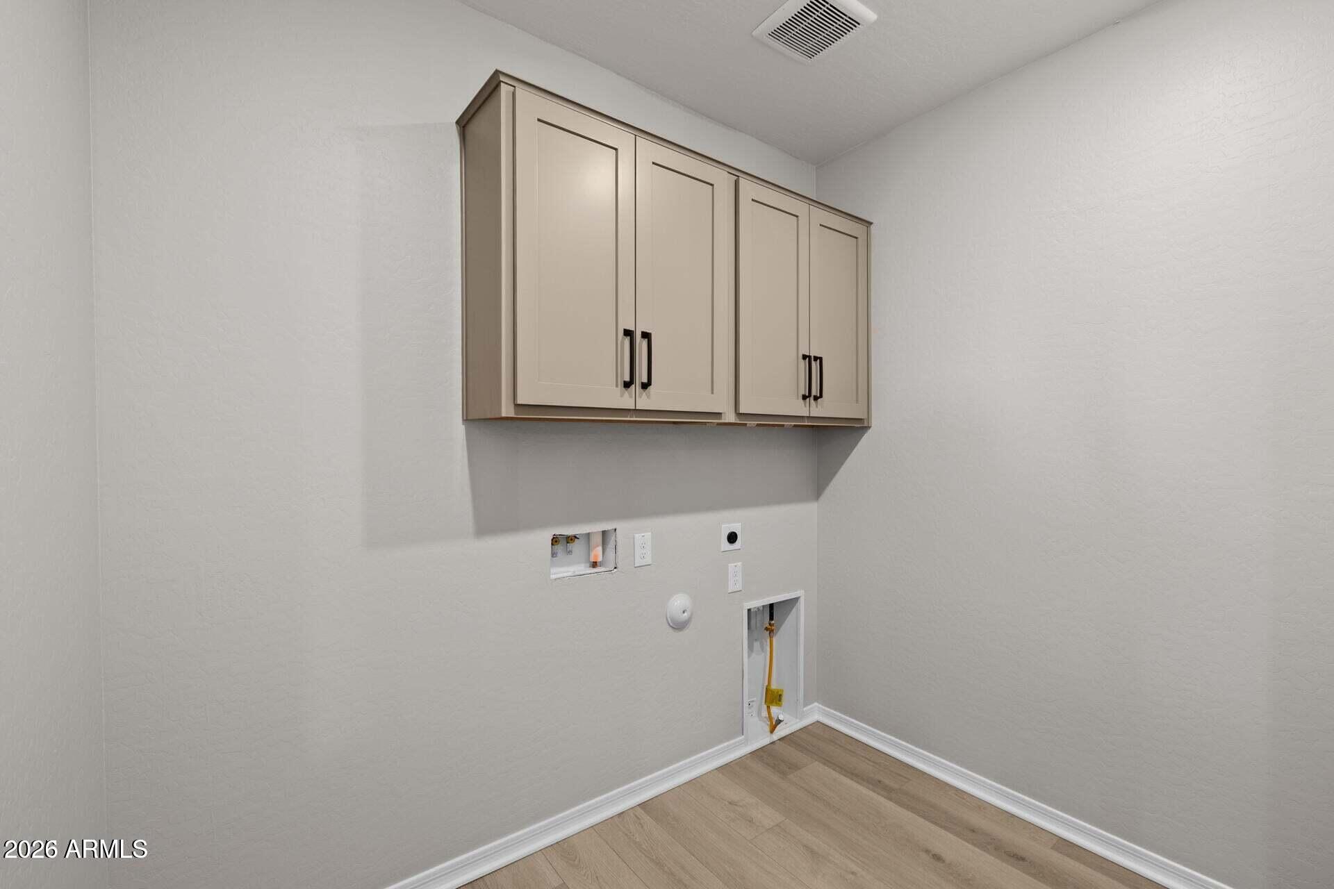Empty laundry room with upper cabinets, washer and dryer hookups, and light wood-look flooring.