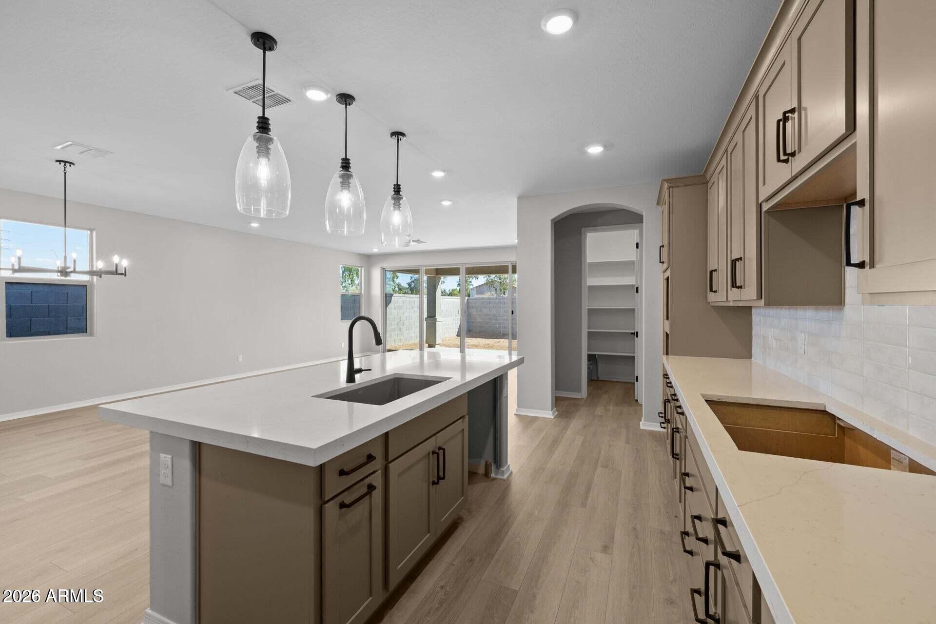 Unfurnished kitchen with a large sink island, taupe cabinets, and sliding glass doors to the backyard.