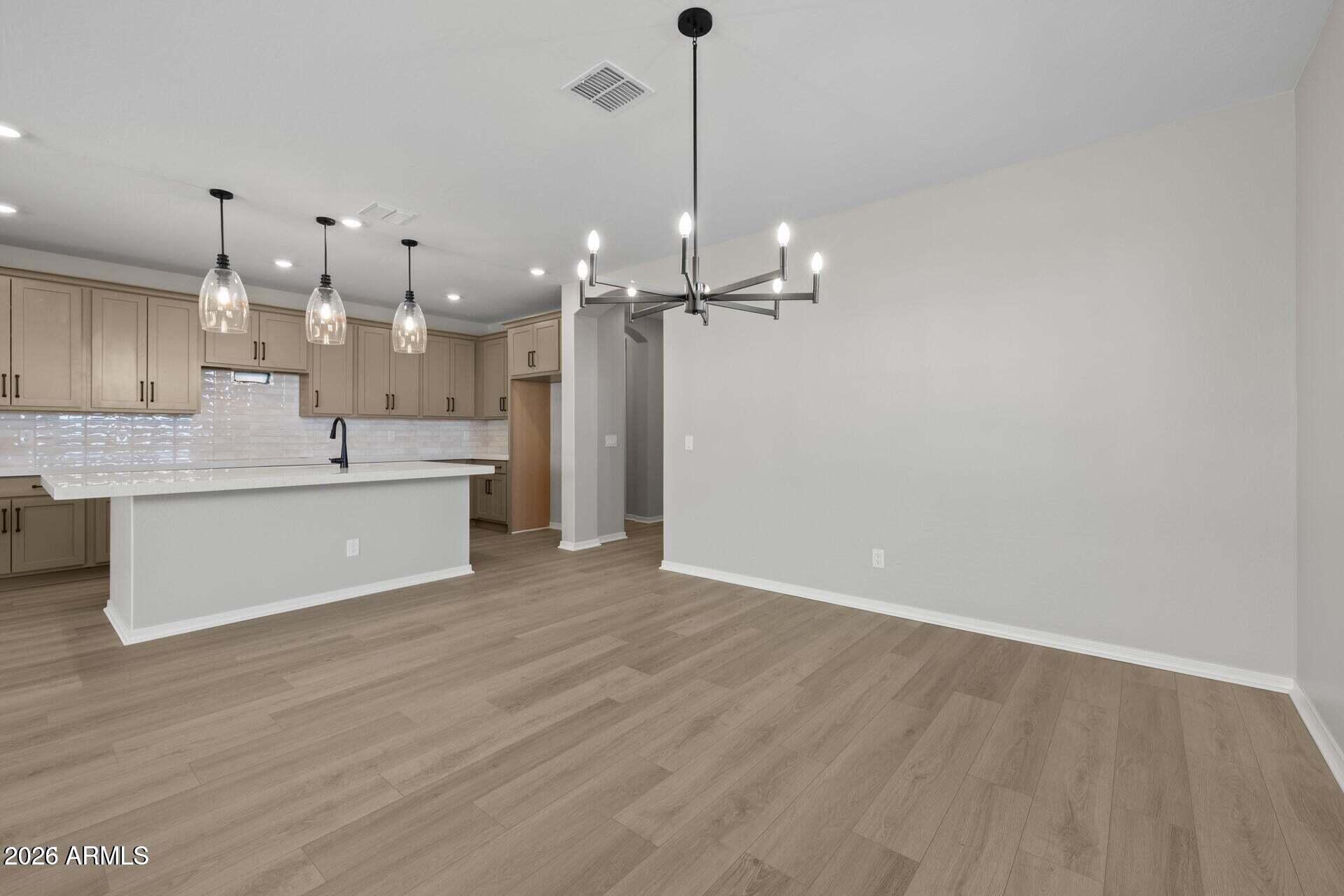 Open kitchen and dining area with a white island, taupe cabinets, and wood-look flooring.