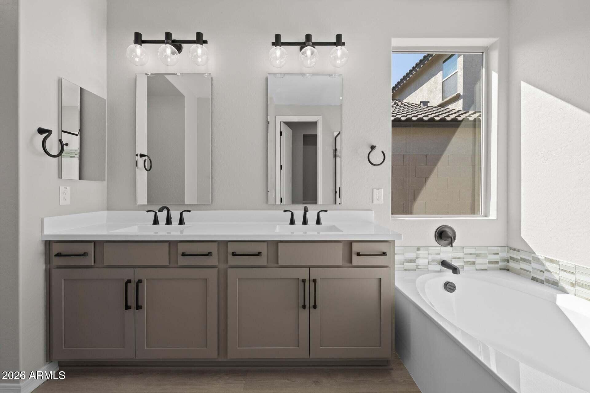 Bathroom with a double vanity and soaking tub beside a sunlit window.