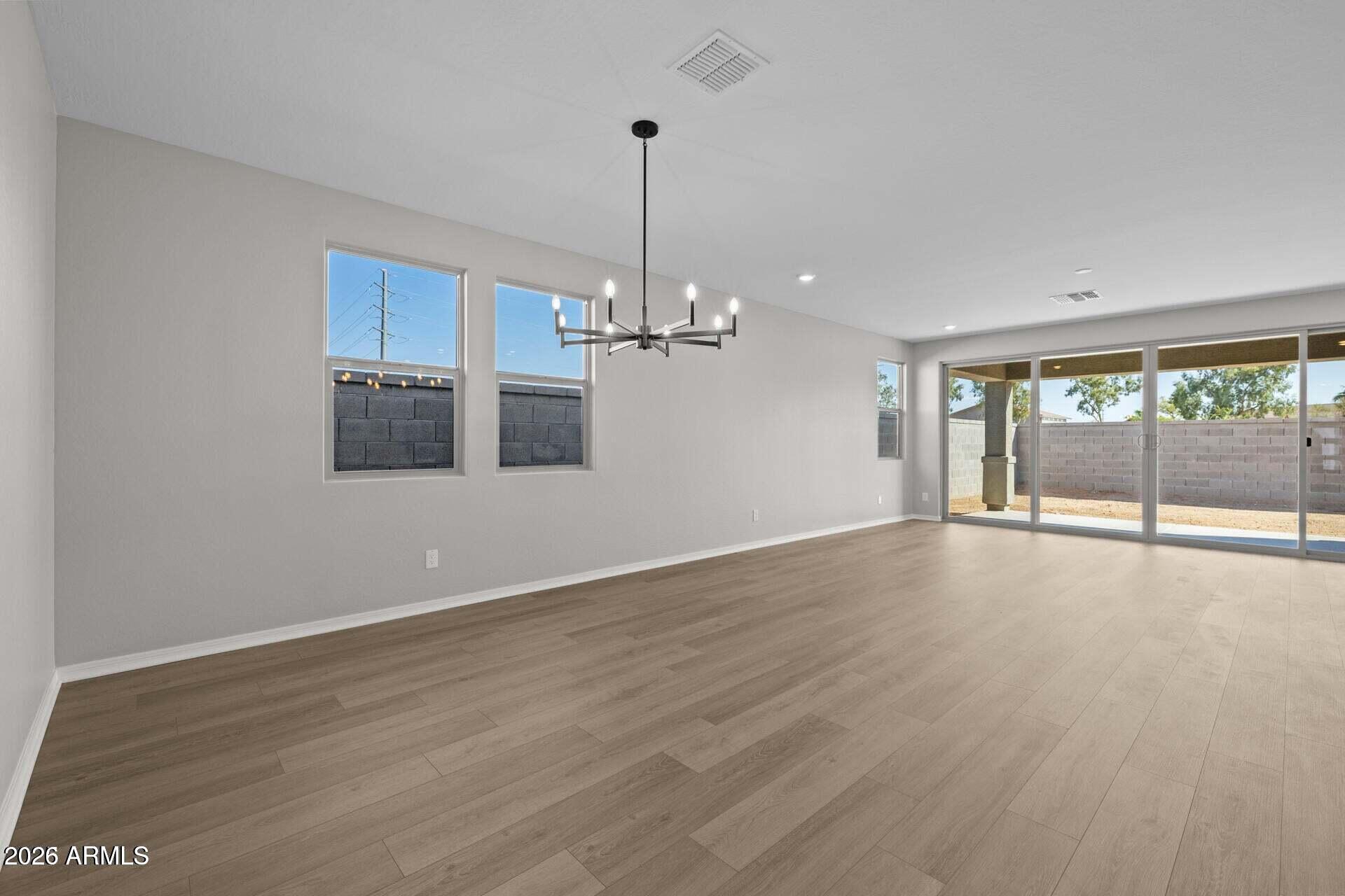 Empty open living area with wood-look floors, a modern chandelier, and sliding glass doors to the patio.