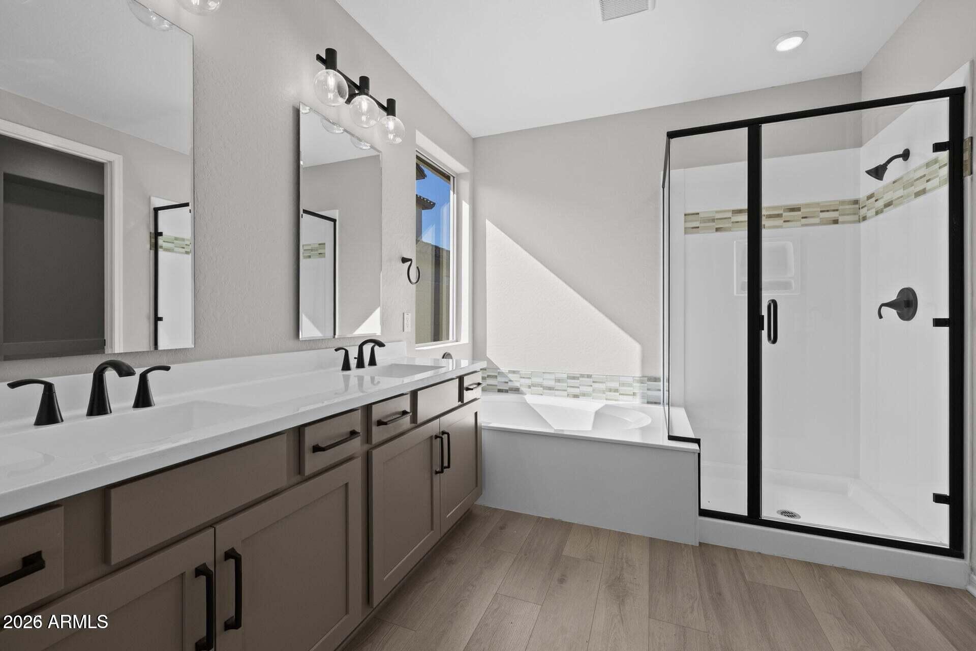 Bathroom with a double vanity, built-in tub, and black-framed glass shower.