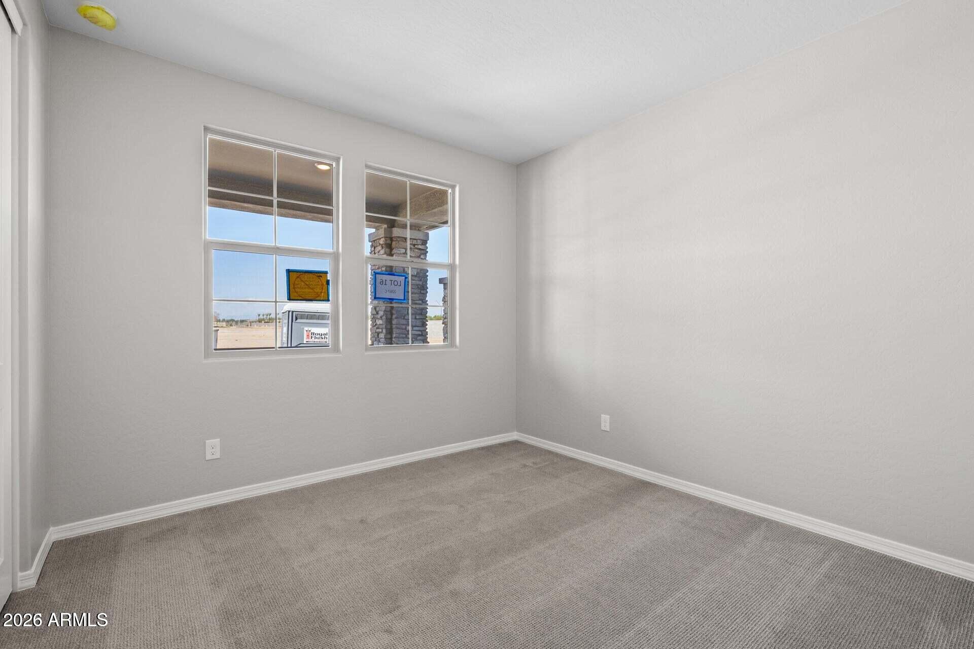 Empty carpeted room with gray walls and two divided-pane windows overlooking a stone porch column.