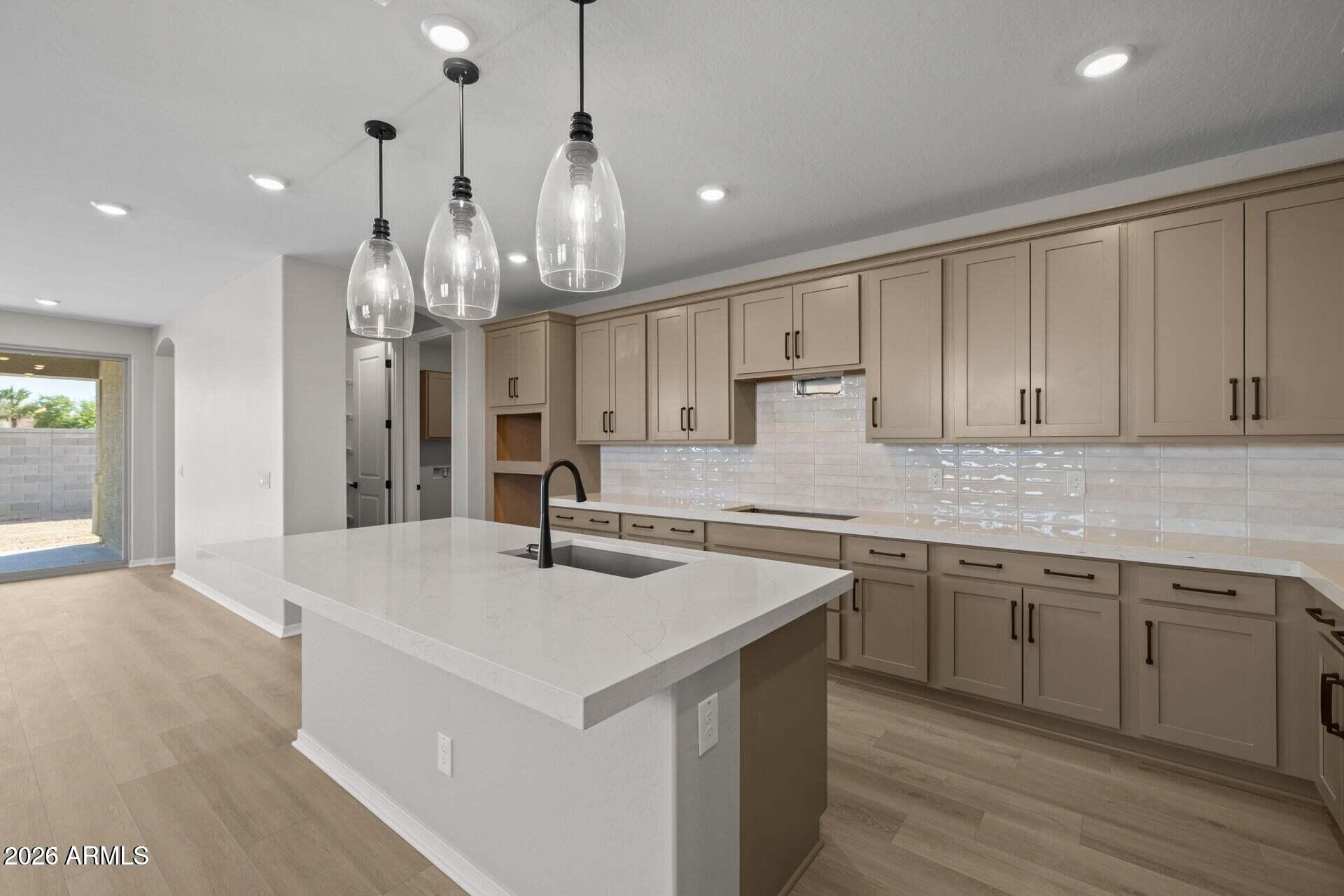 Kitchen with a large white island, taupe cabinets, glossy tile backsplash, and glass pendant lights.