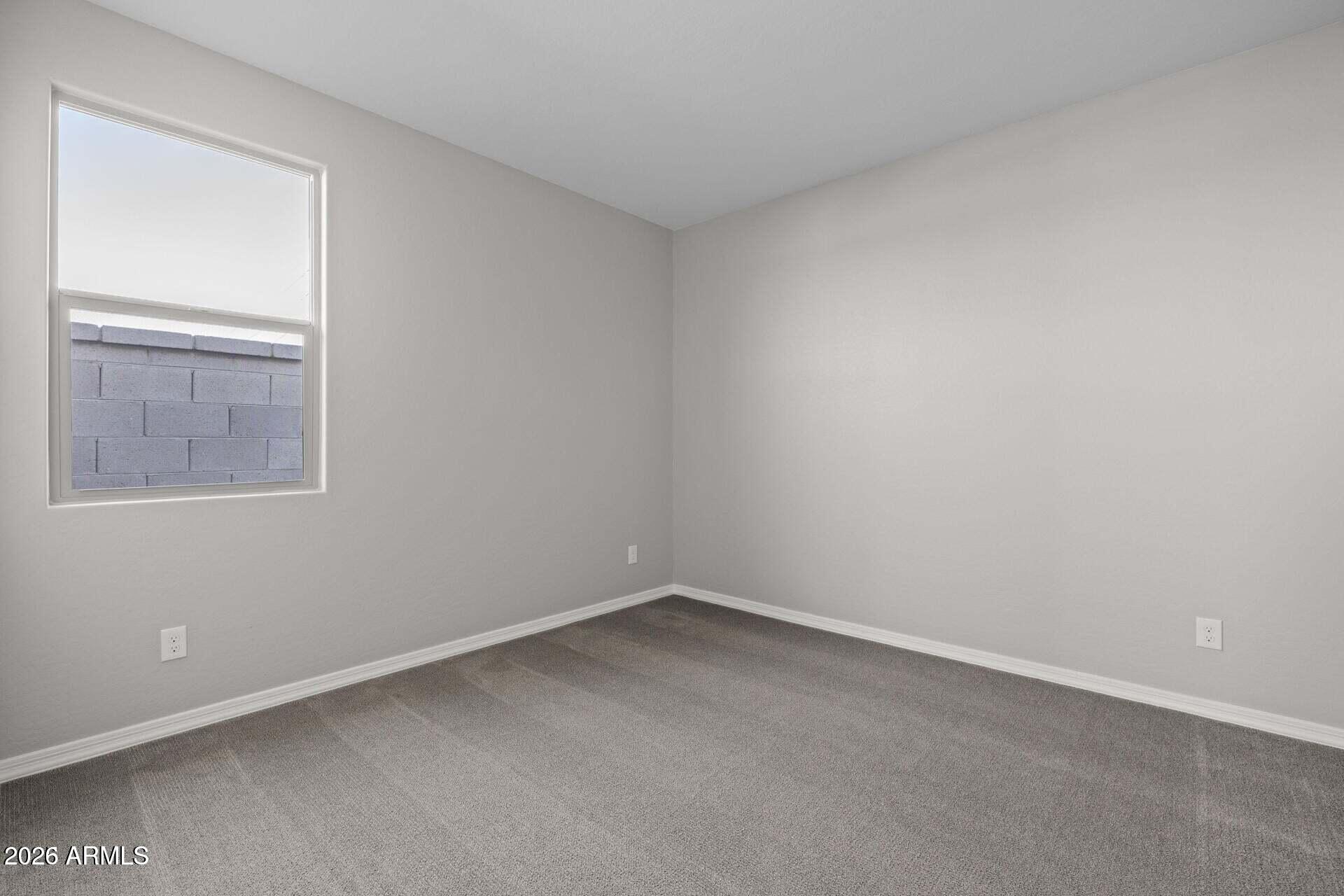 Empty carpeted room with gray walls and a window overlooking a block wall.