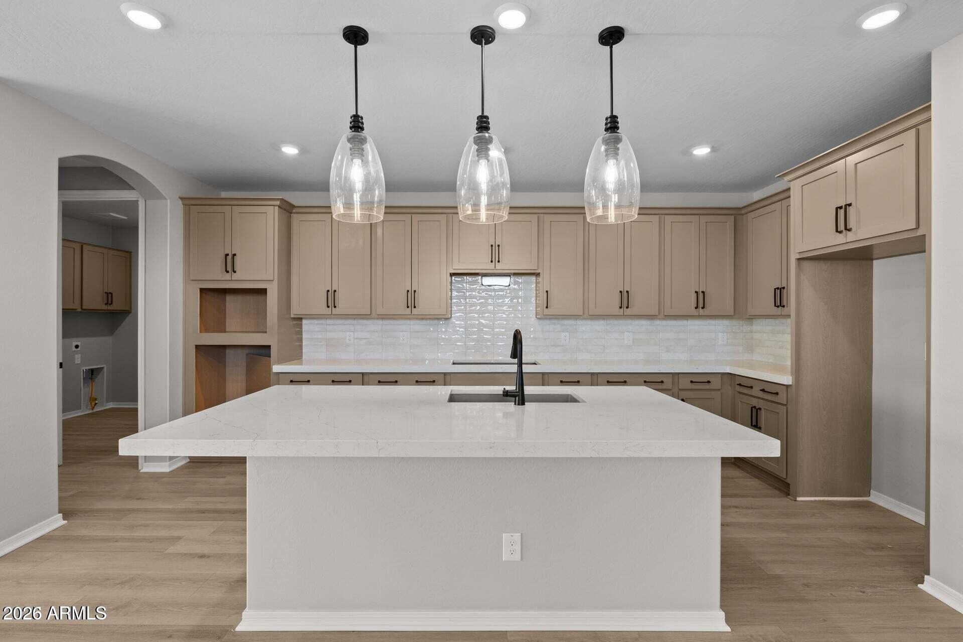 Vacant kitchen with a large white island, taupe cabinets, and three glass pendant lights.