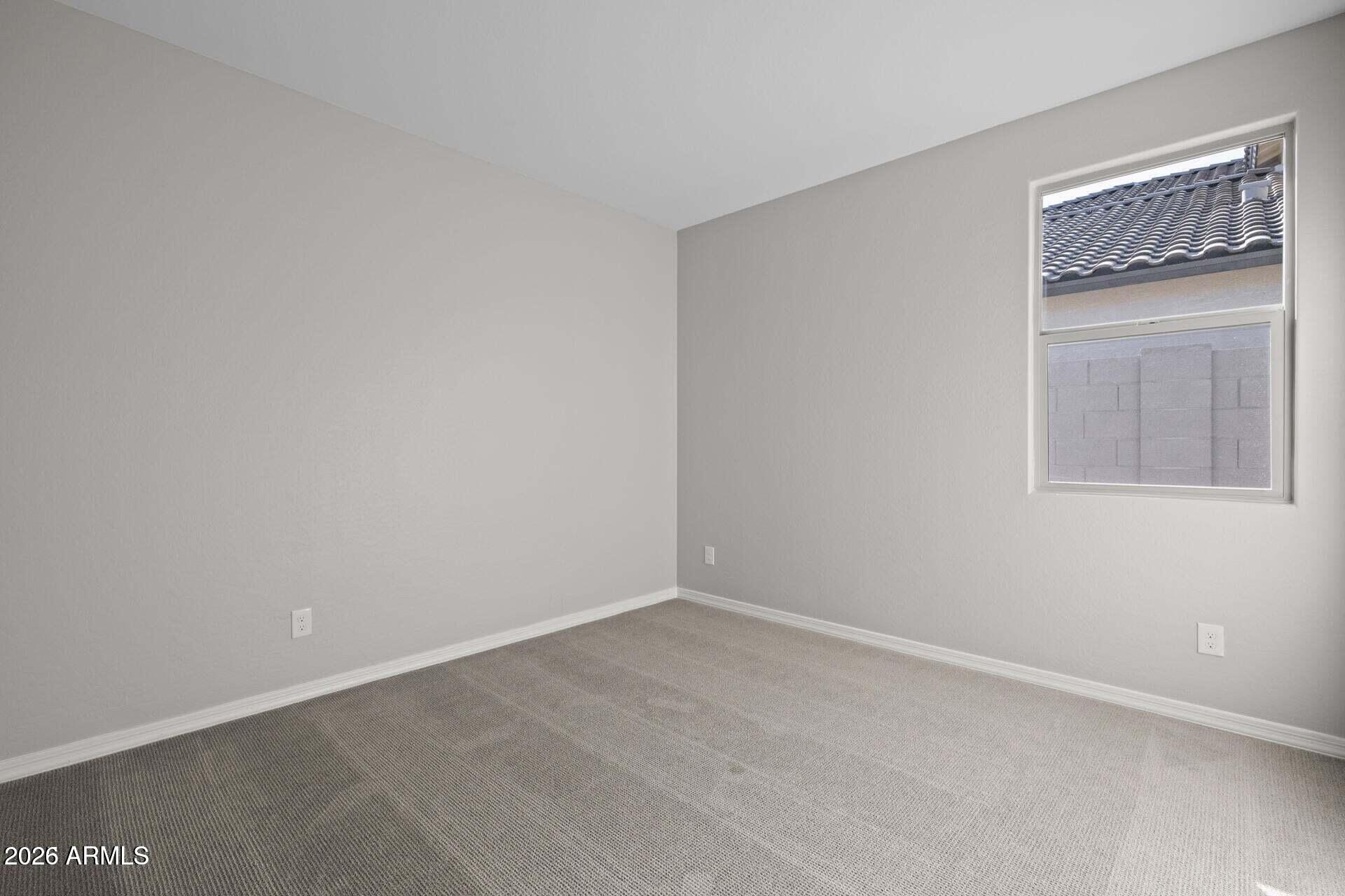 Empty bedroom with beige carpet, light gray walls, and a window facing a tiled roof.