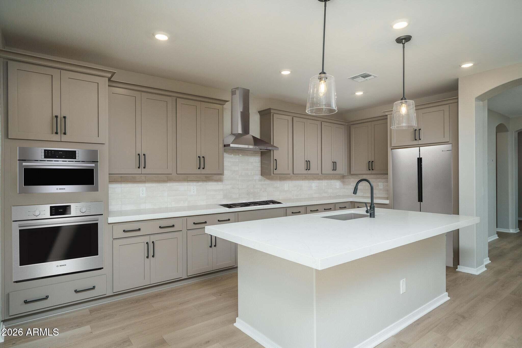 Kitchen with taupe cabinets, stainless-steel appliances, white tile backsplash and a large white island.