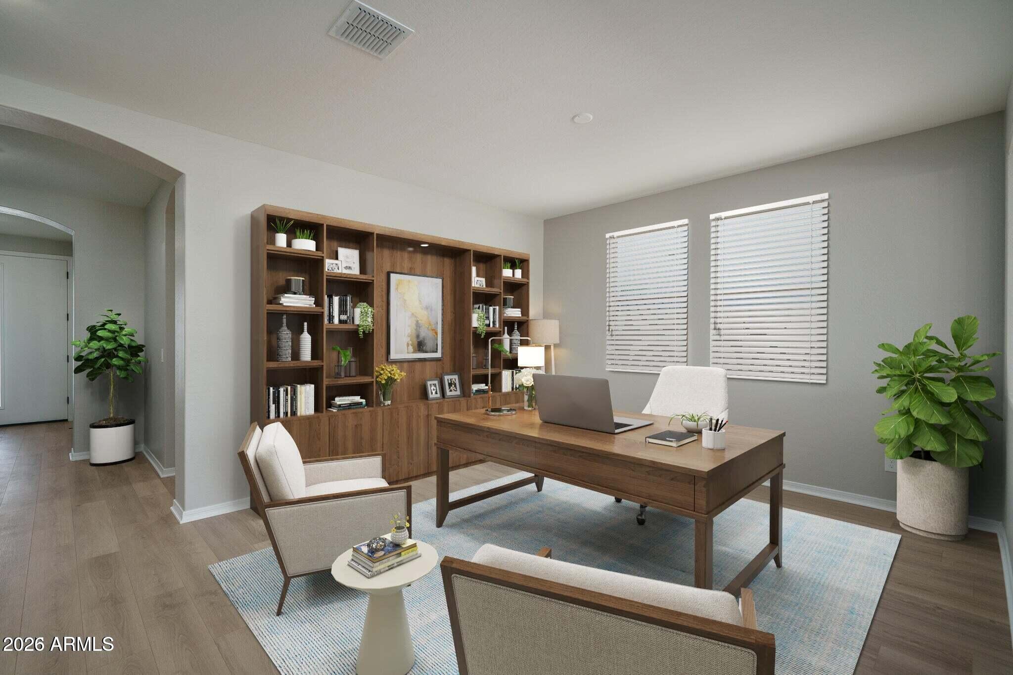 Home office with a wooden desk, built-in bookcases, laptop, and neutral armchairs.